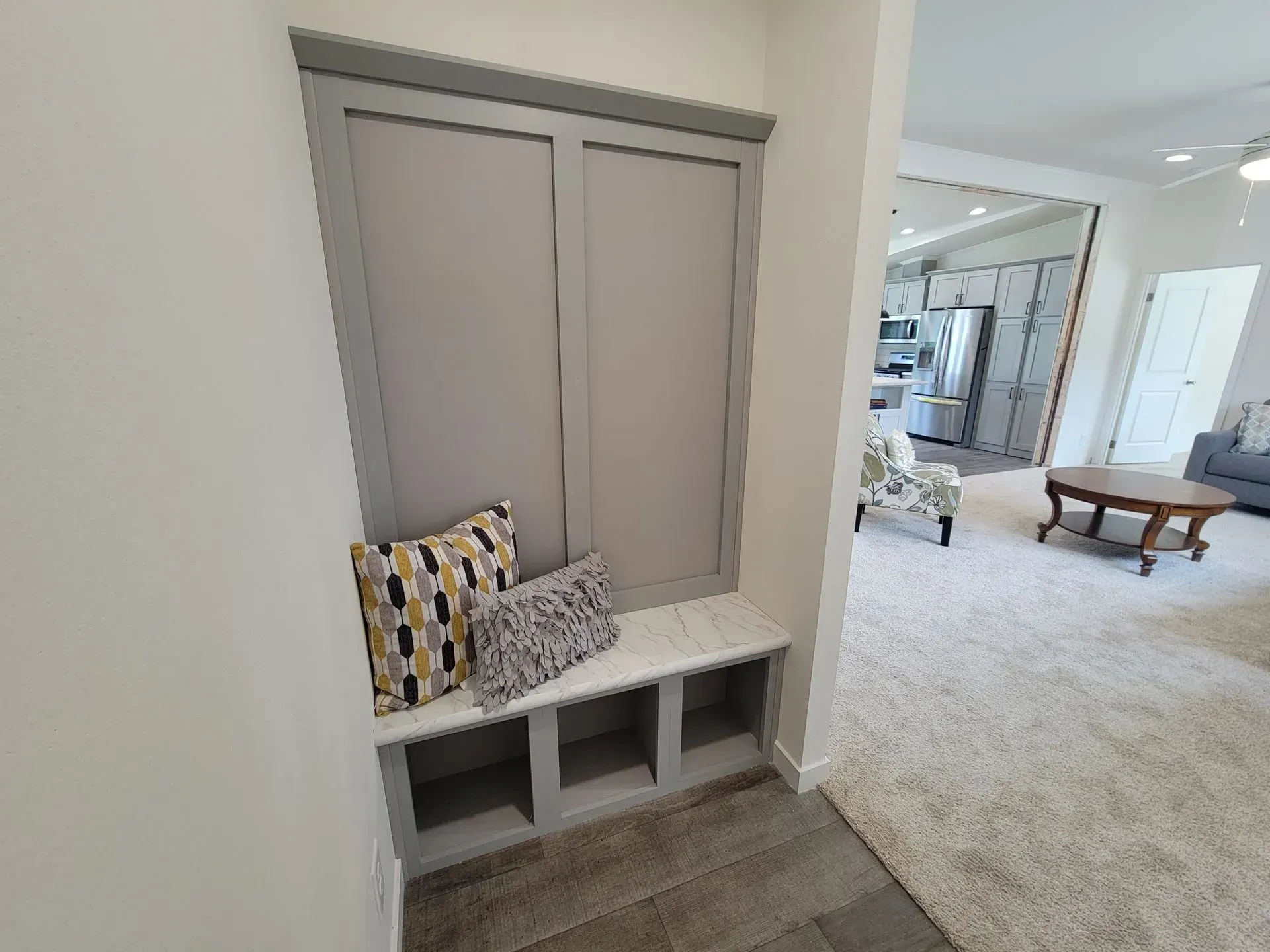 Built-in bench with storage and gray cabinet doors, two pillows, and a view of a living room.