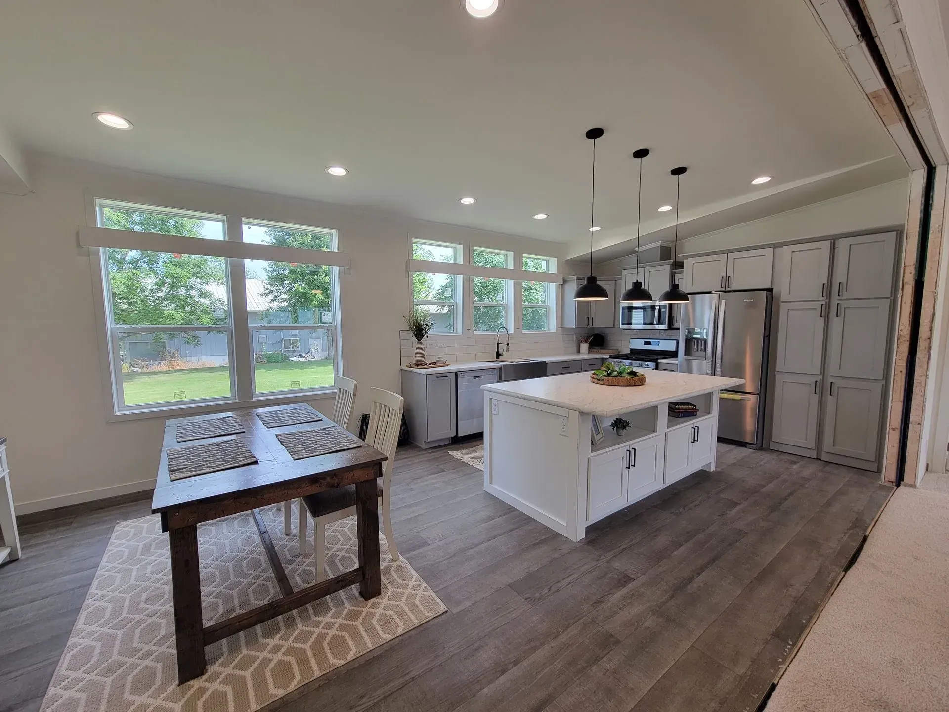 Spacious kitchen with island, gray cabinets, stainless steel appliances, and dining table by windows.