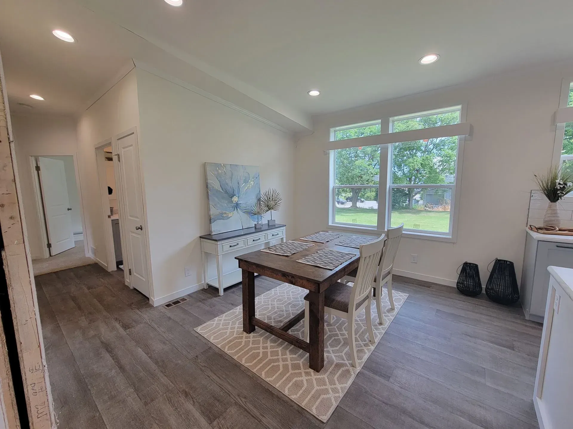 Dining room with wooden table, rug, window, and white walls.