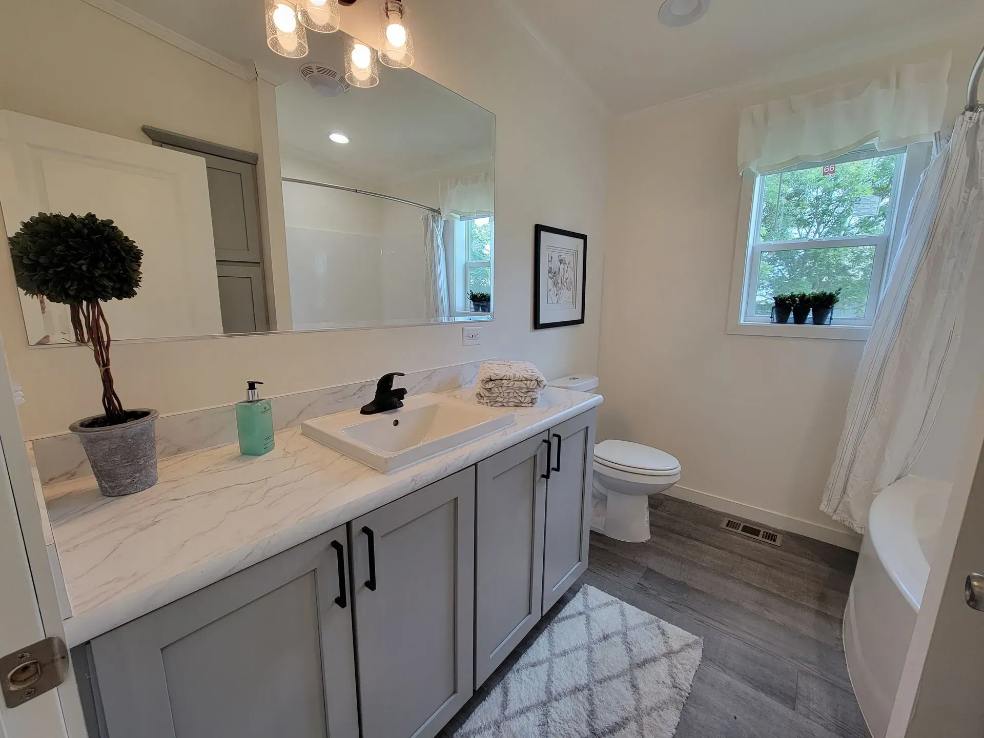 Bathroom with gray cabinets, white countertop, large mirror, and small rug.