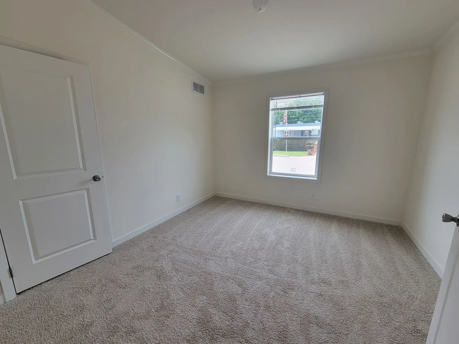 Empty room with white walls, a closed door, window, and beige carpet.