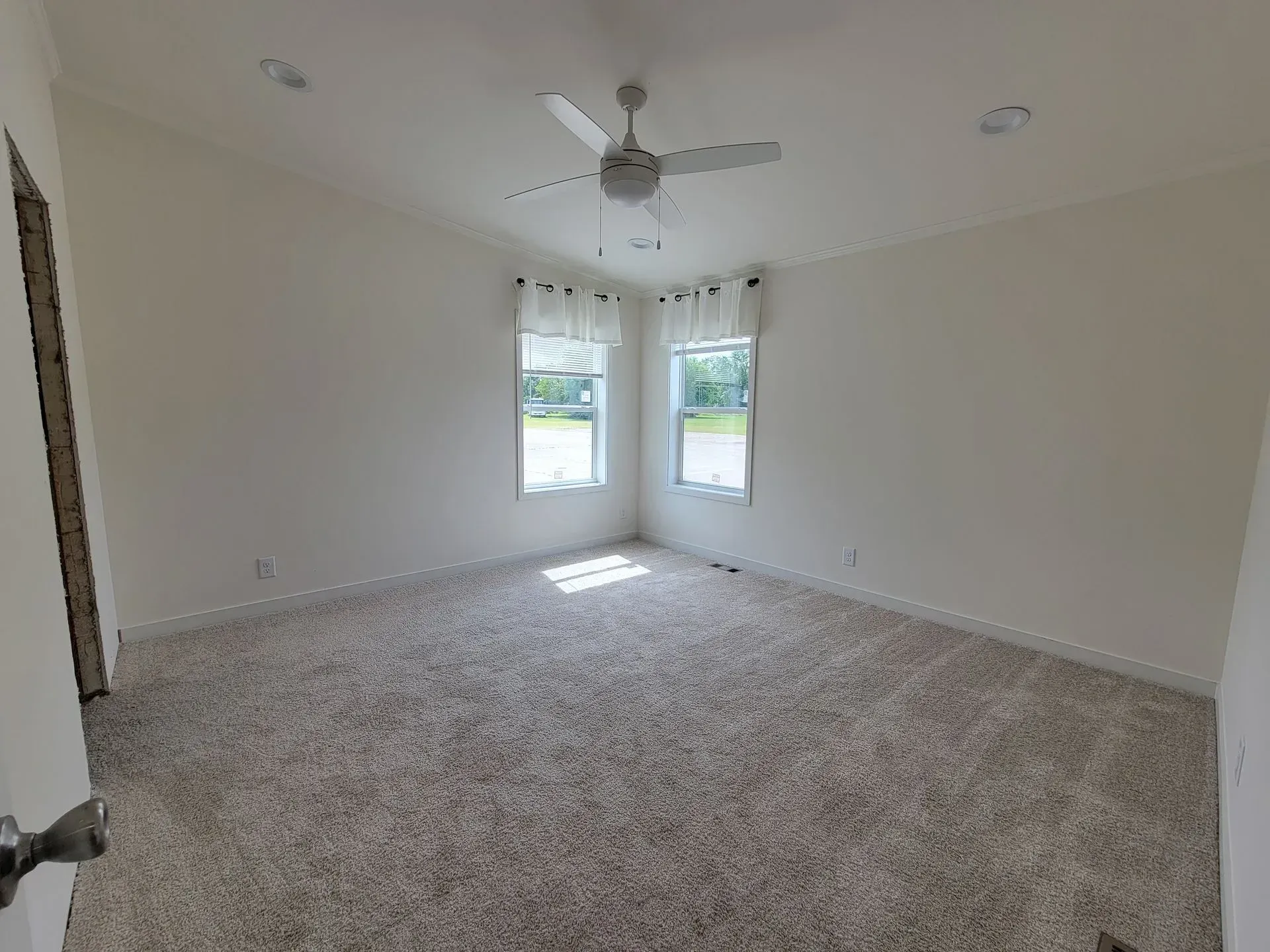 Empty bedroom with light beige carpet, white walls, two windows, and a ceiling fan.