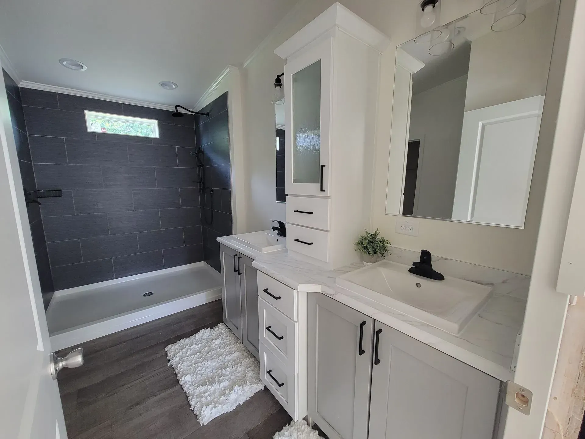 Modern bathroom with gray tiled shower, double vanity, and white cabinets.