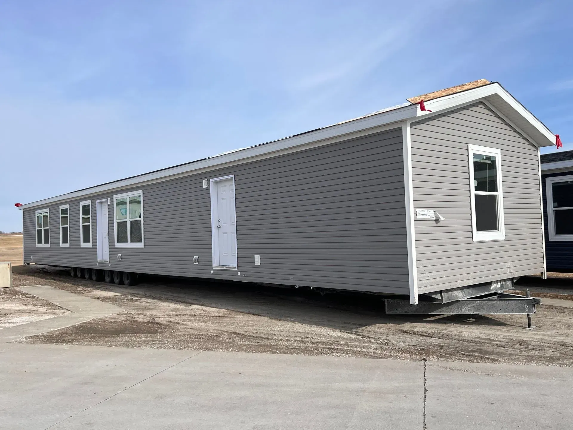 Gray manufactured home on a concrete surface, with white trim and a blue sky.