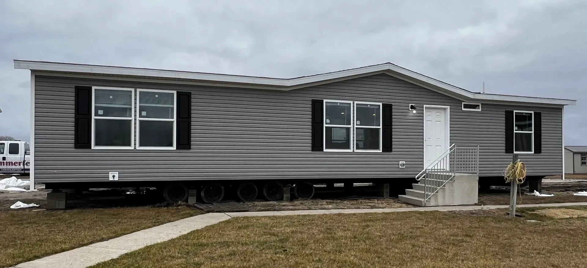 A gray mobile home with black shutters and a white front door, set on a brown grassy field.