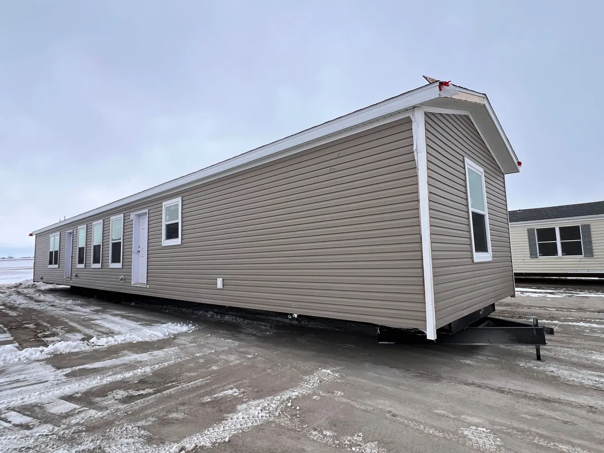 Tan mobile home with white trim on a snowy lot.