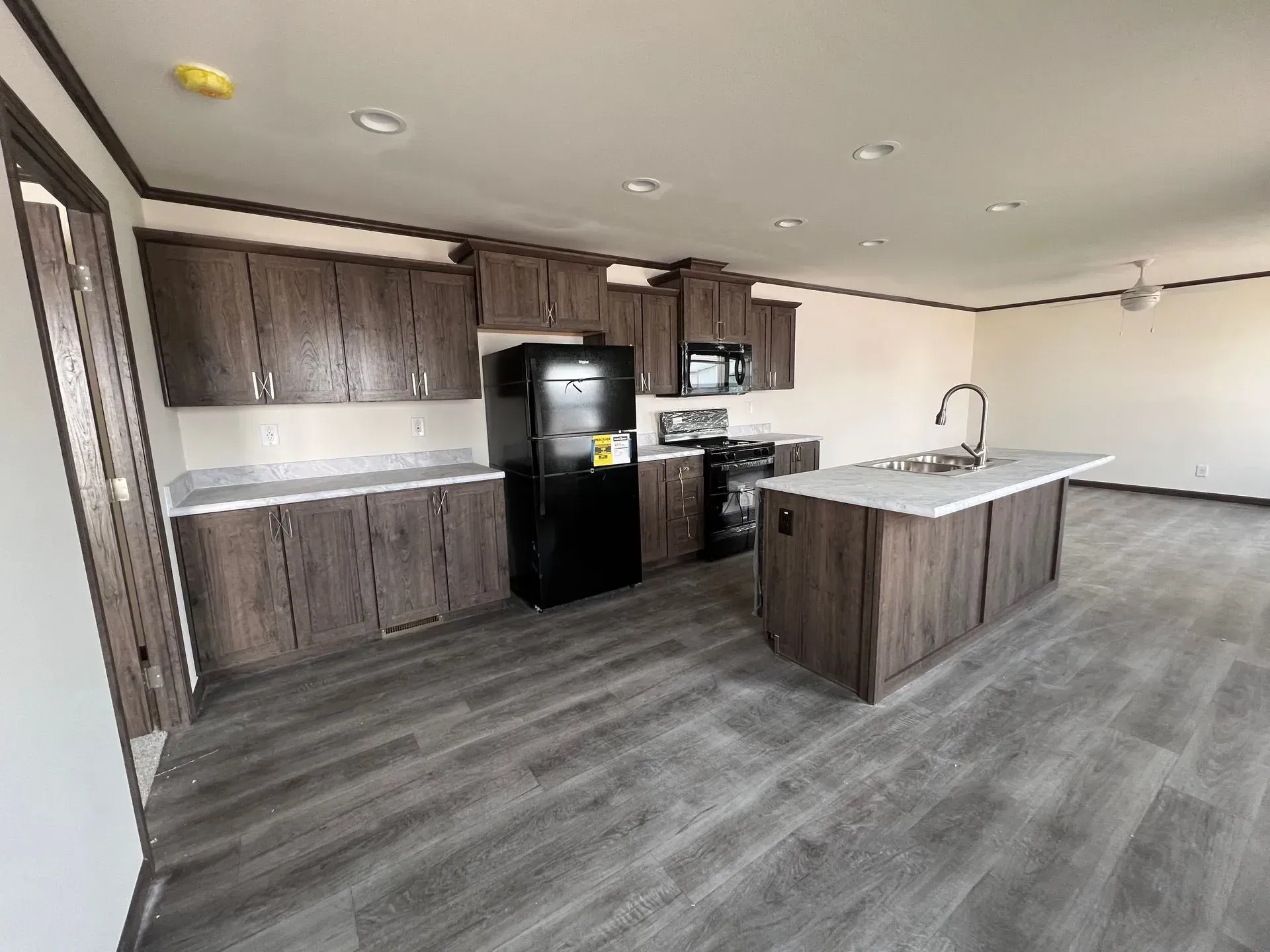 Kitchen with dark brown cabinets, black appliances, and gray flooring. Island with sink.