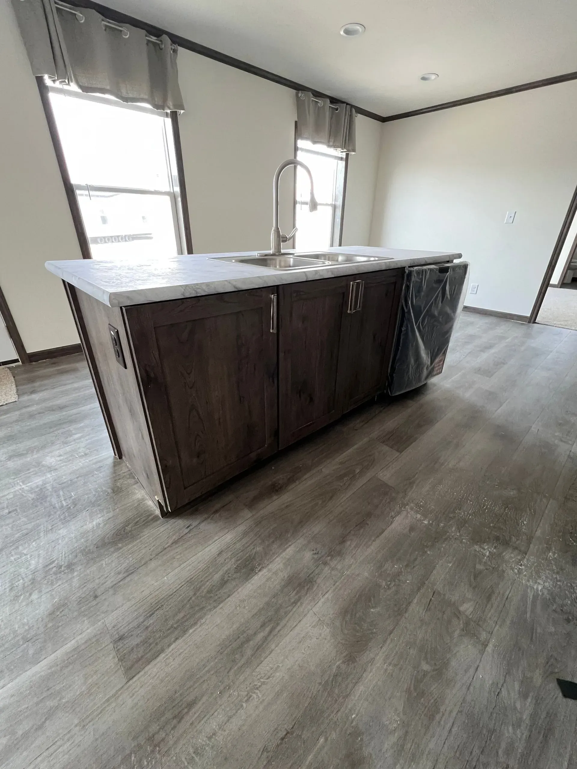 Kitchen island with sink, dishwasher, and wood-grain cabinets in a room with hardwood floors and windows.