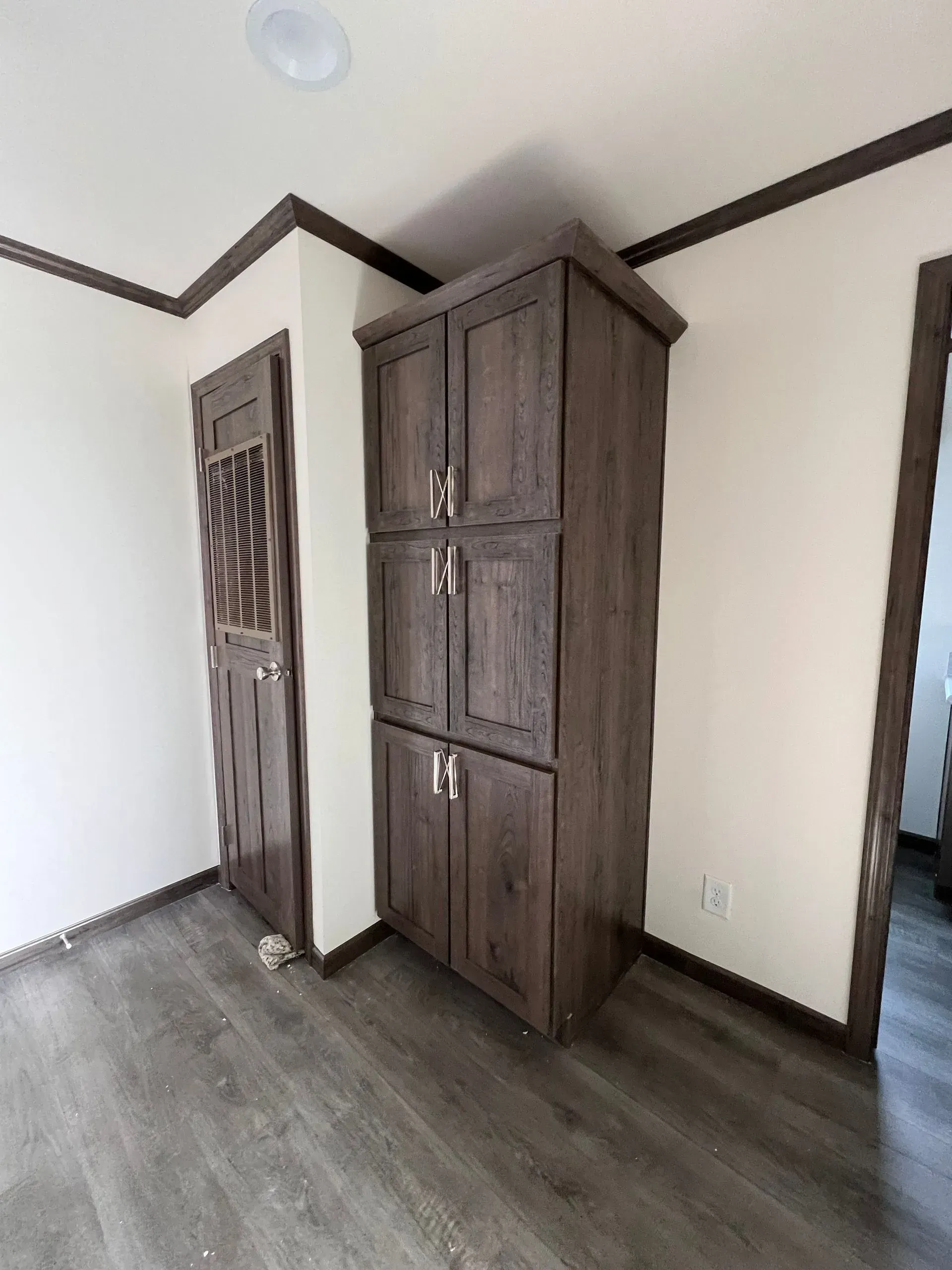 Tall, dark wooden pantry cabinet and door in a room with light walls and dark trim.