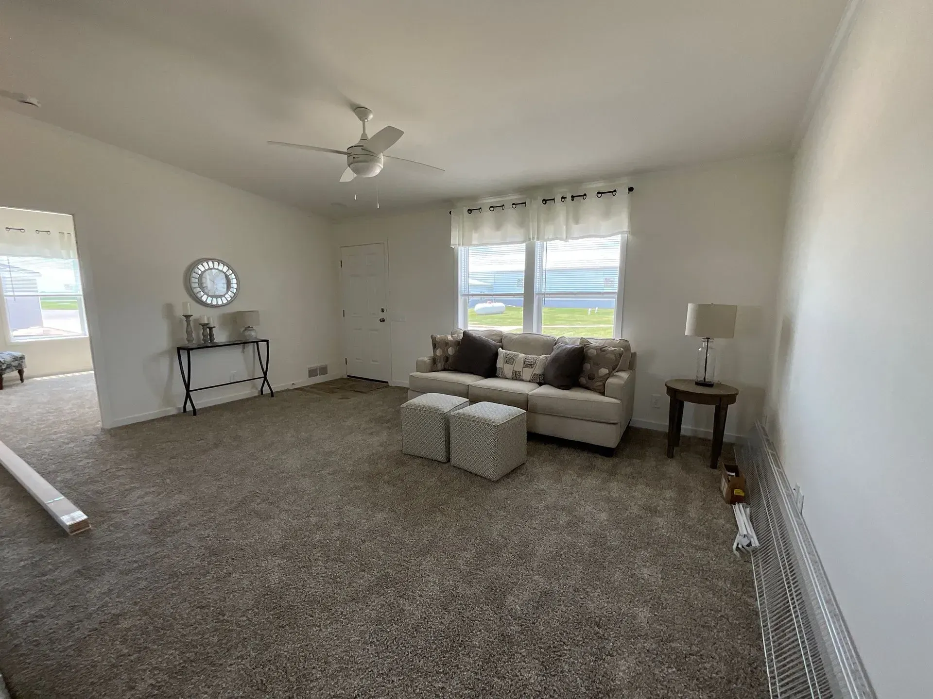 Living room with neutral tones, beige sofa, ottomans, and a round mirror on a table.