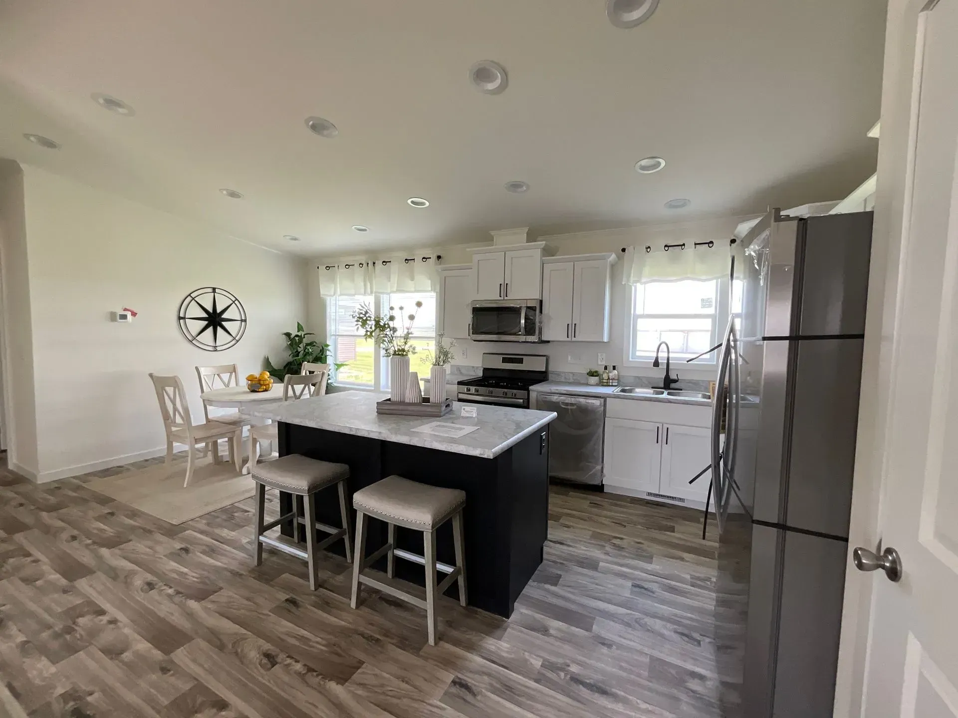 Modern kitchen with island, white cabinets, and stainless steel appliances. Dining table in the background.