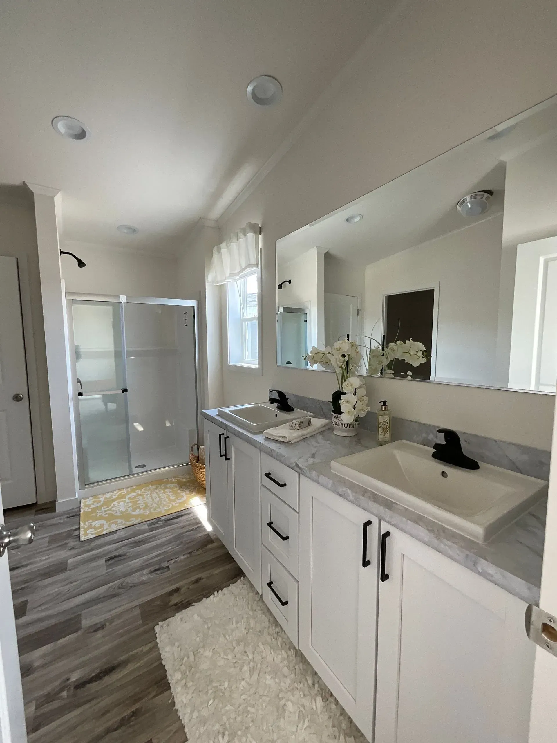 Bright bathroom with white vanity, large mirror, and glass shower.
