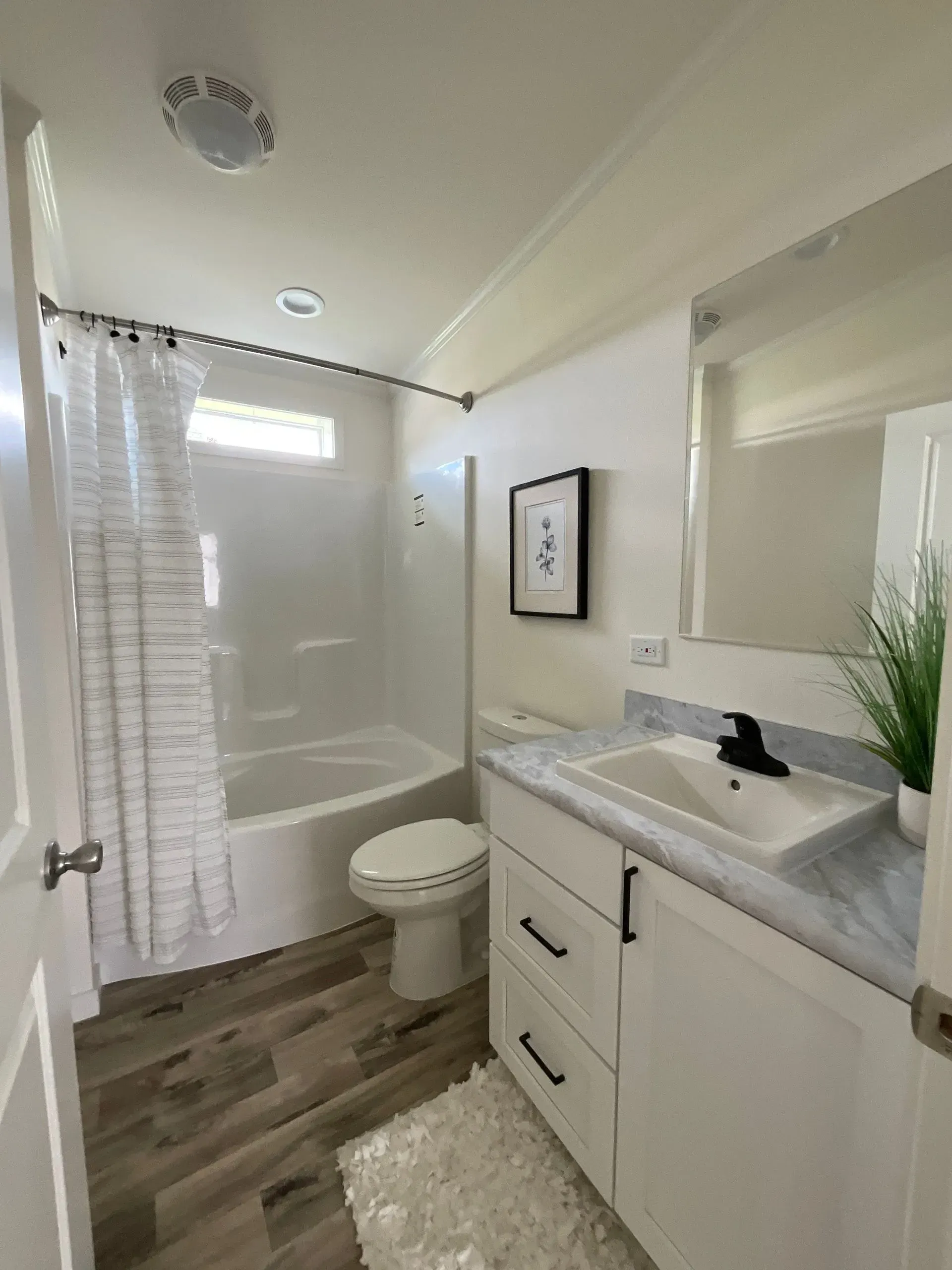 Bathroom with white walls, vanity, toilet, and shower/tub.  Wood-look floor, and a small rug.