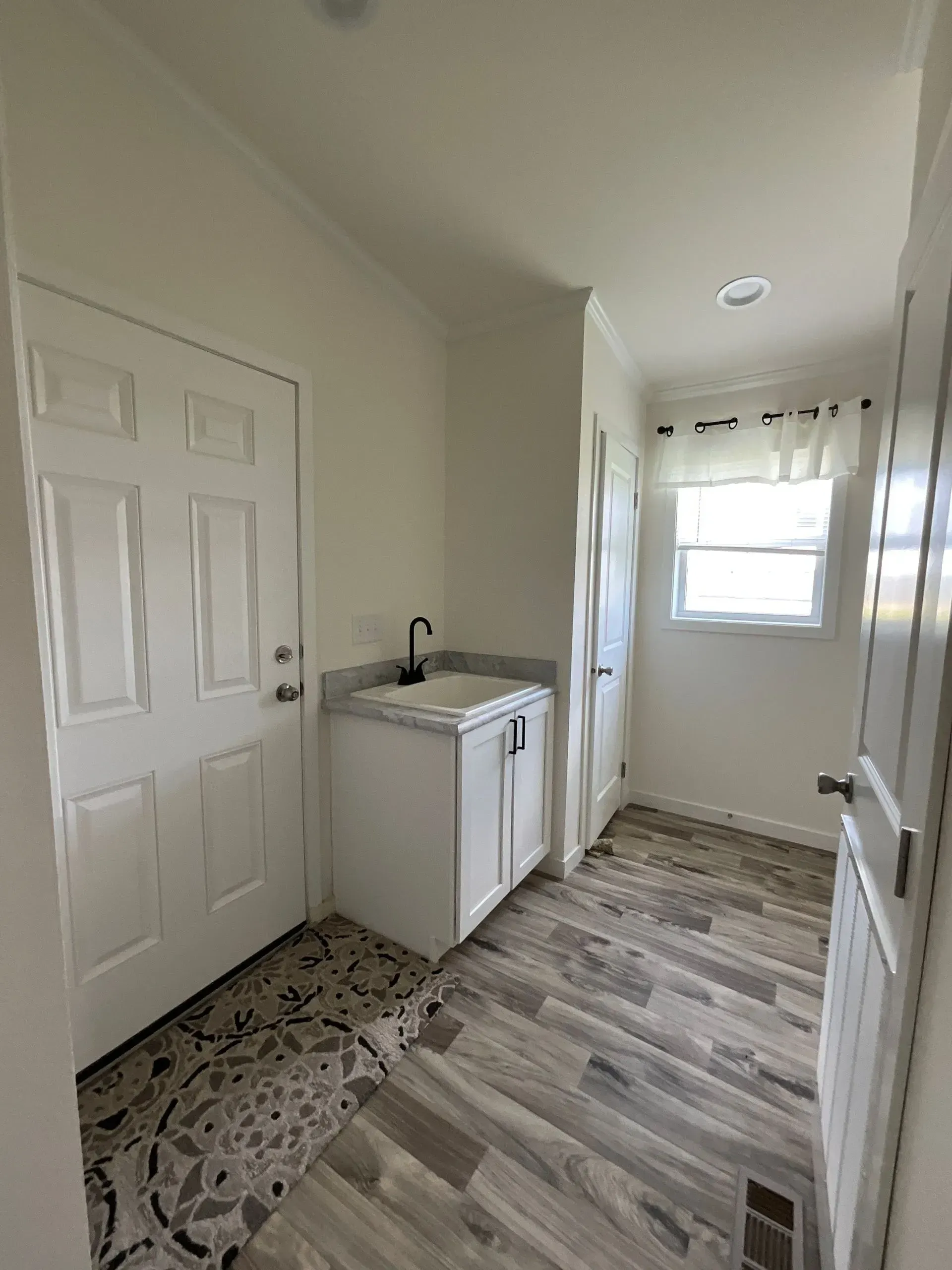 White laundry room with door, sink, window, and wood-look flooring.