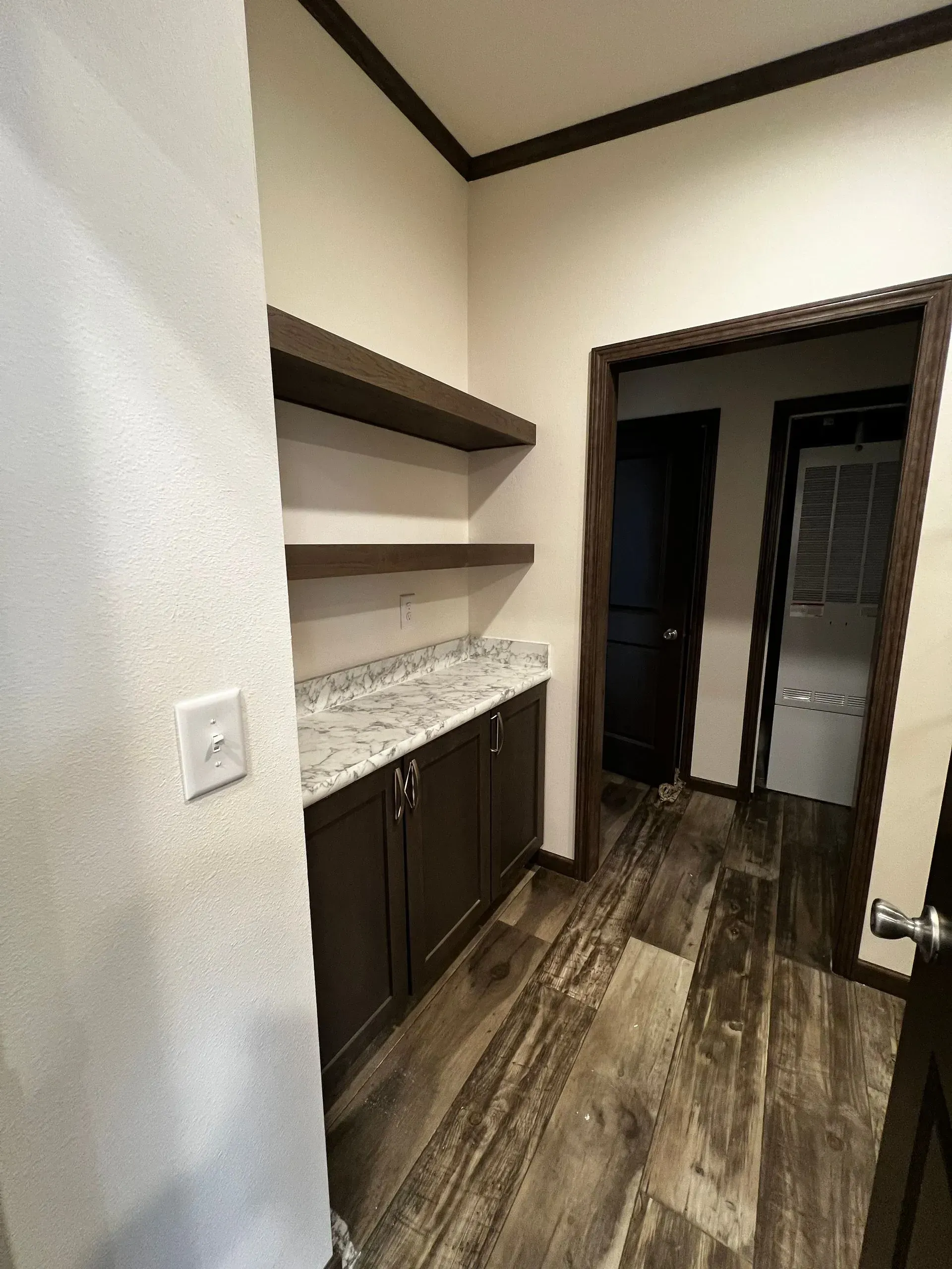 Pantry with wooden shelves, cabinets, and granite countertop. Dark brown trim and flooring. Doorways lead to other rooms.