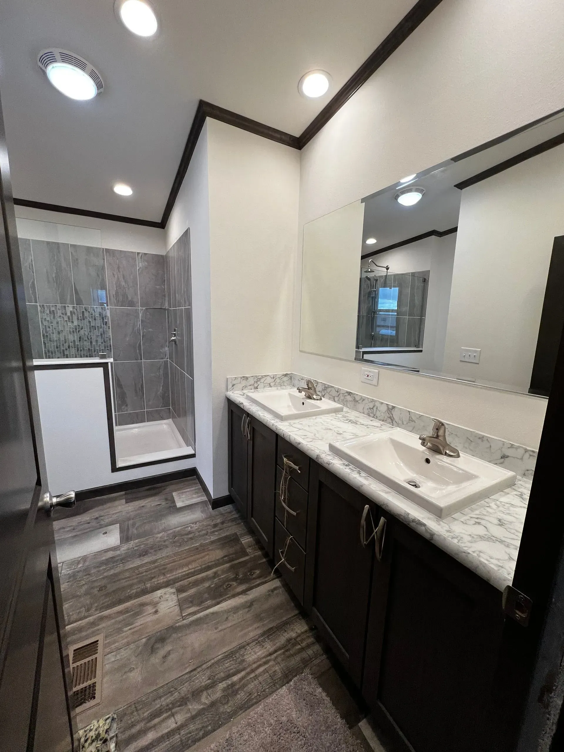 Bathroom with dark wood vanity, double sinks, large mirror, and gray tiled shower.