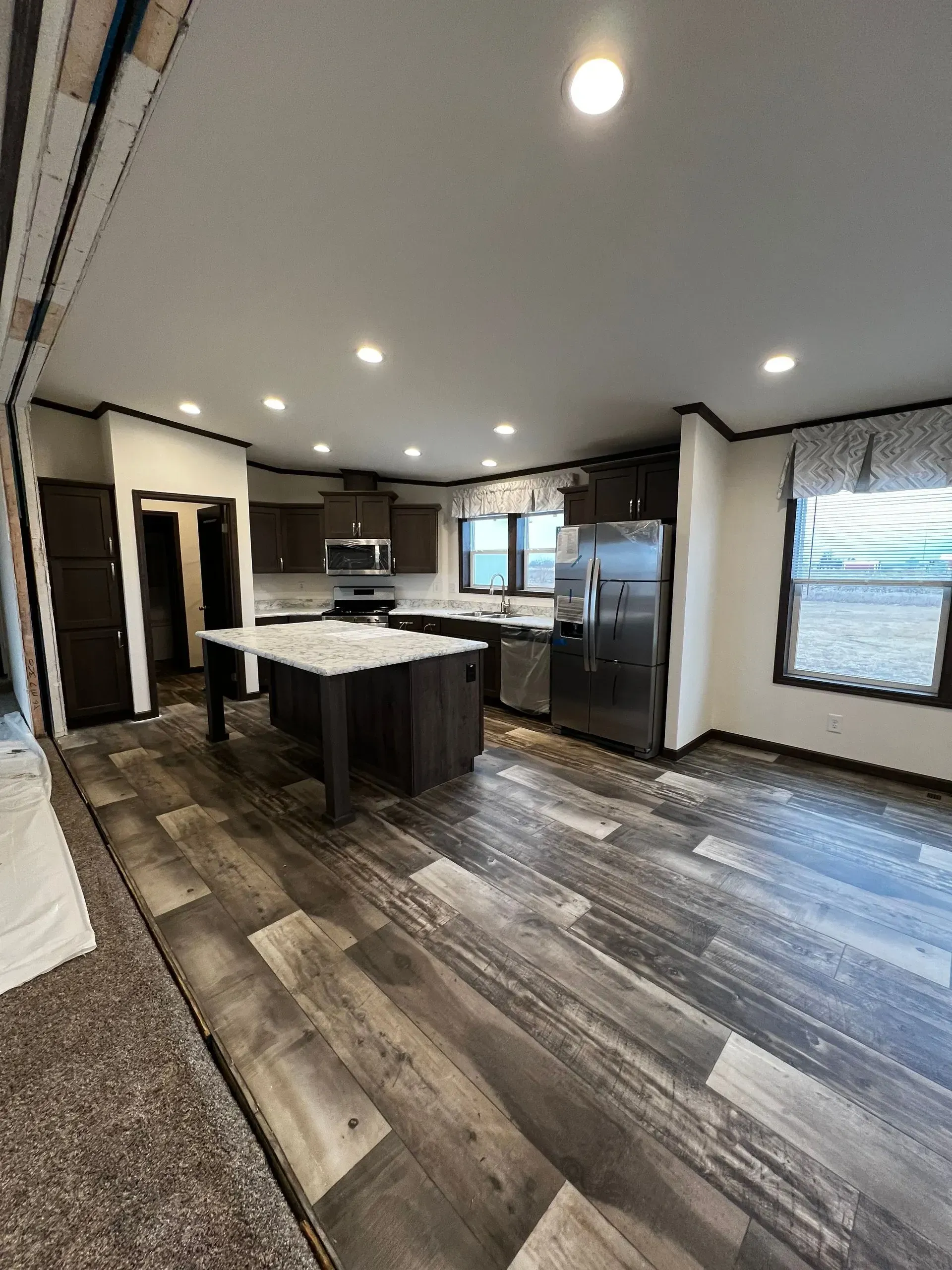 Interior of modern kitchen with dark cabinets, stainless steel appliances, and wood-look flooring.