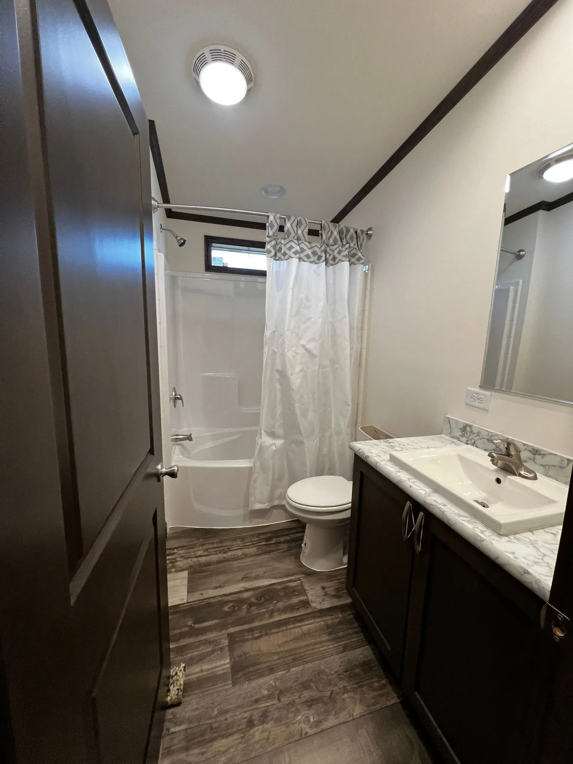 Bathroom with dark brown cabinetry, white sink, tub/shower combo, and patterned shower curtain.