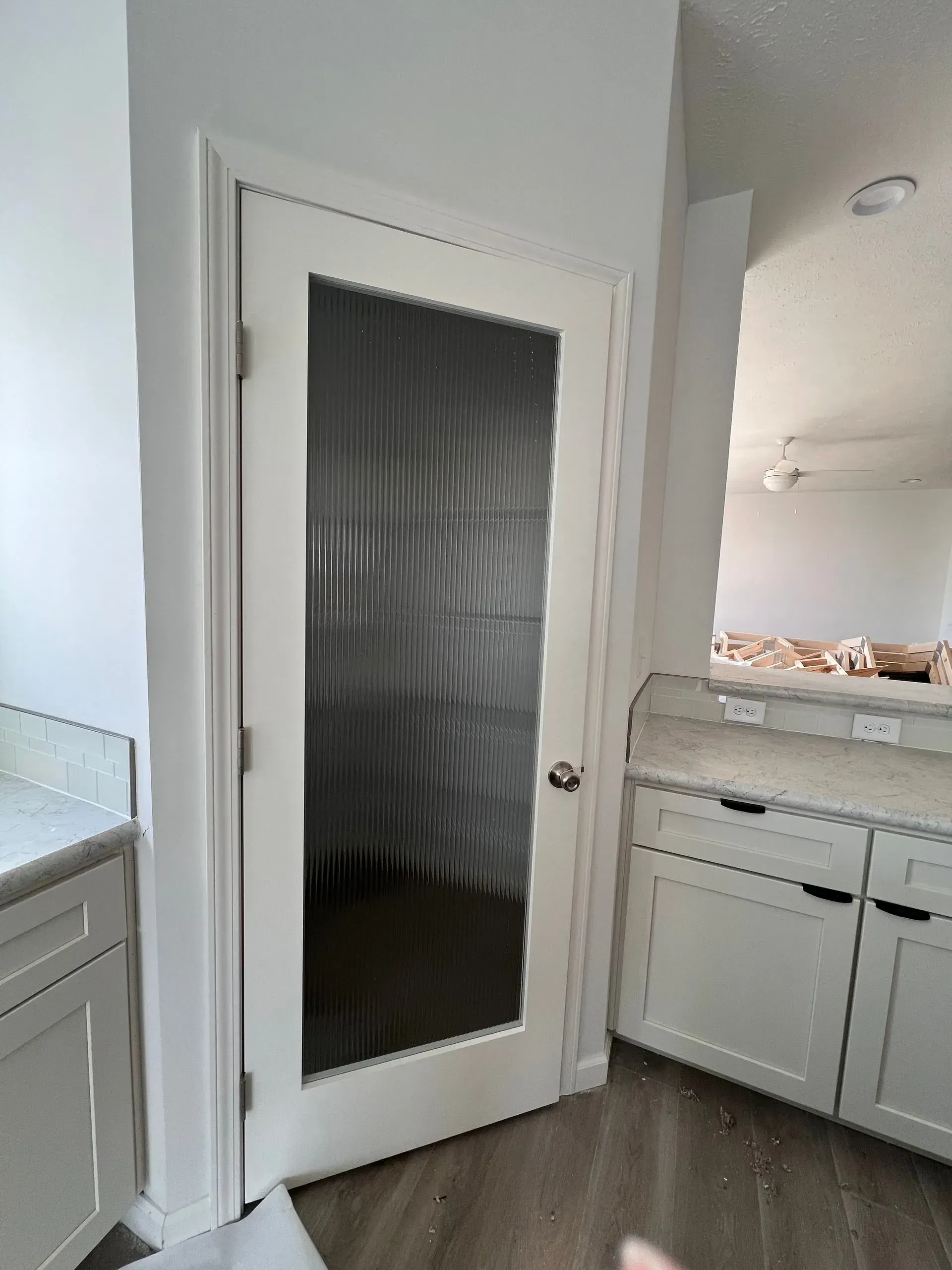 White door with textured glass panel, located between white cabinets and wall.