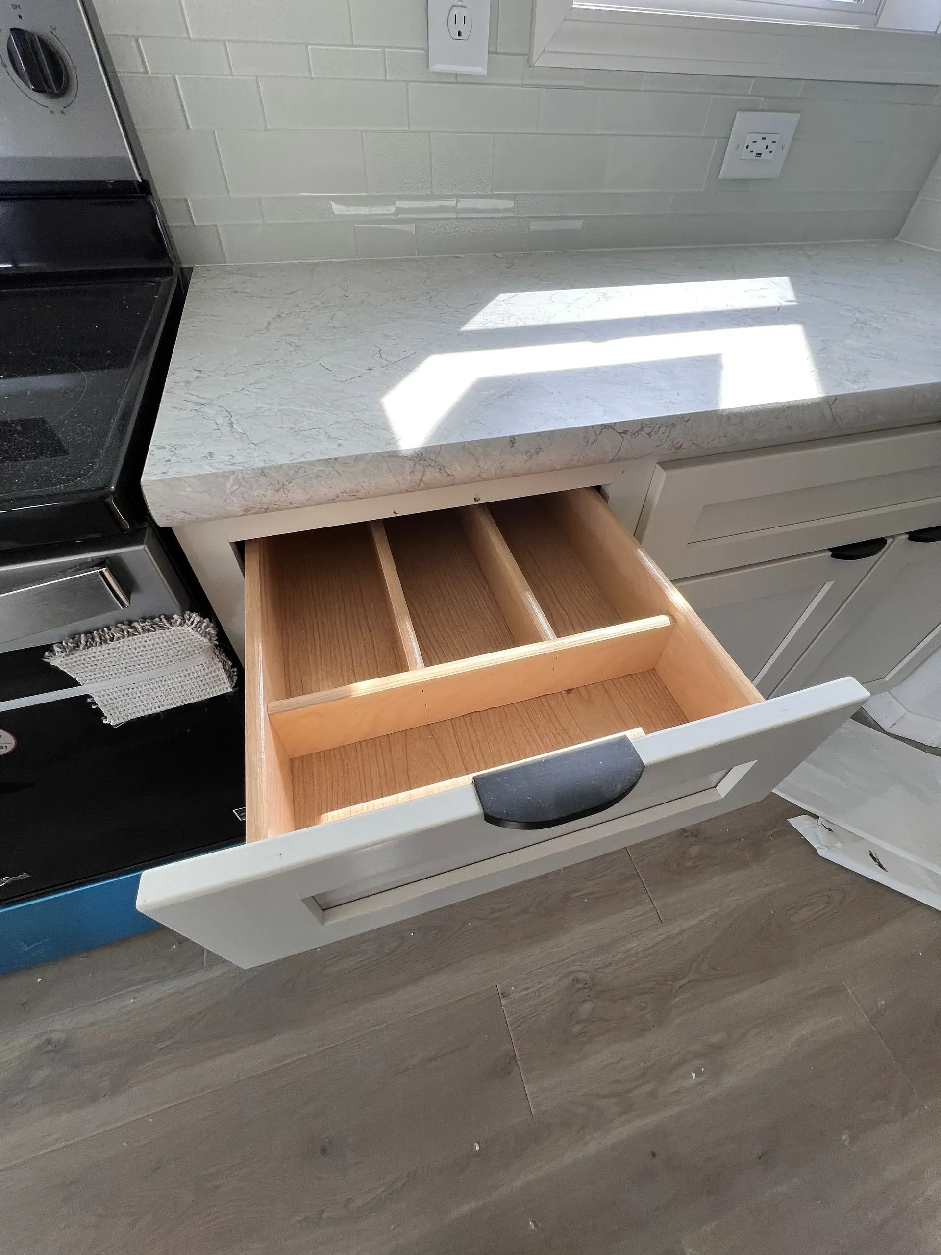 Open kitchen drawer with utensil dividers, near countertop and stove.