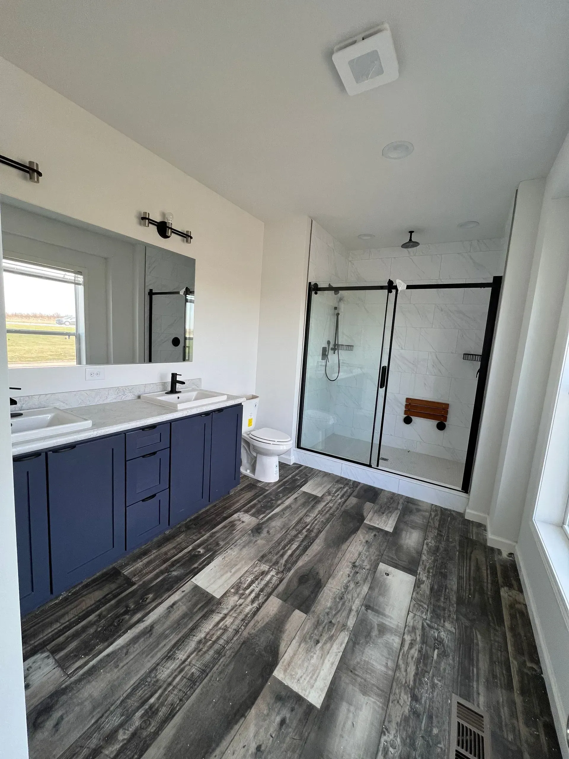 Bathroom with navy vanity, glass shower, and wood-look flooring. White walls and black fixtures.