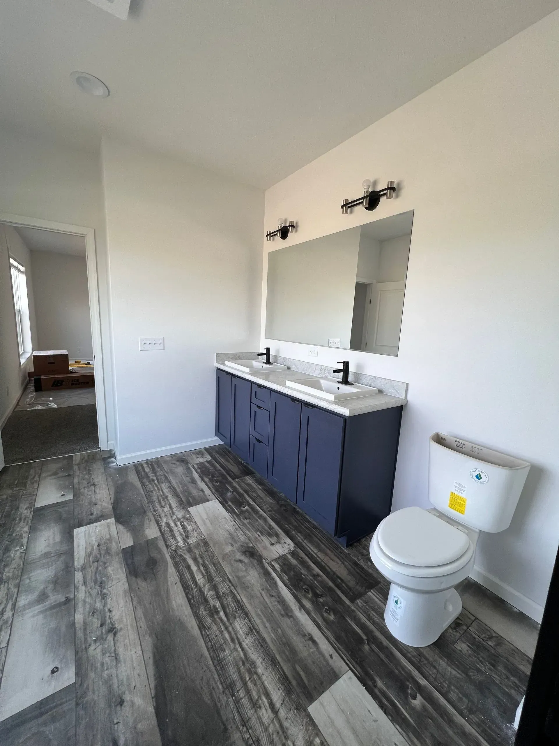 Bathroom with blue vanity, large mirror, and gray wood-look flooring. White walls and toilet.