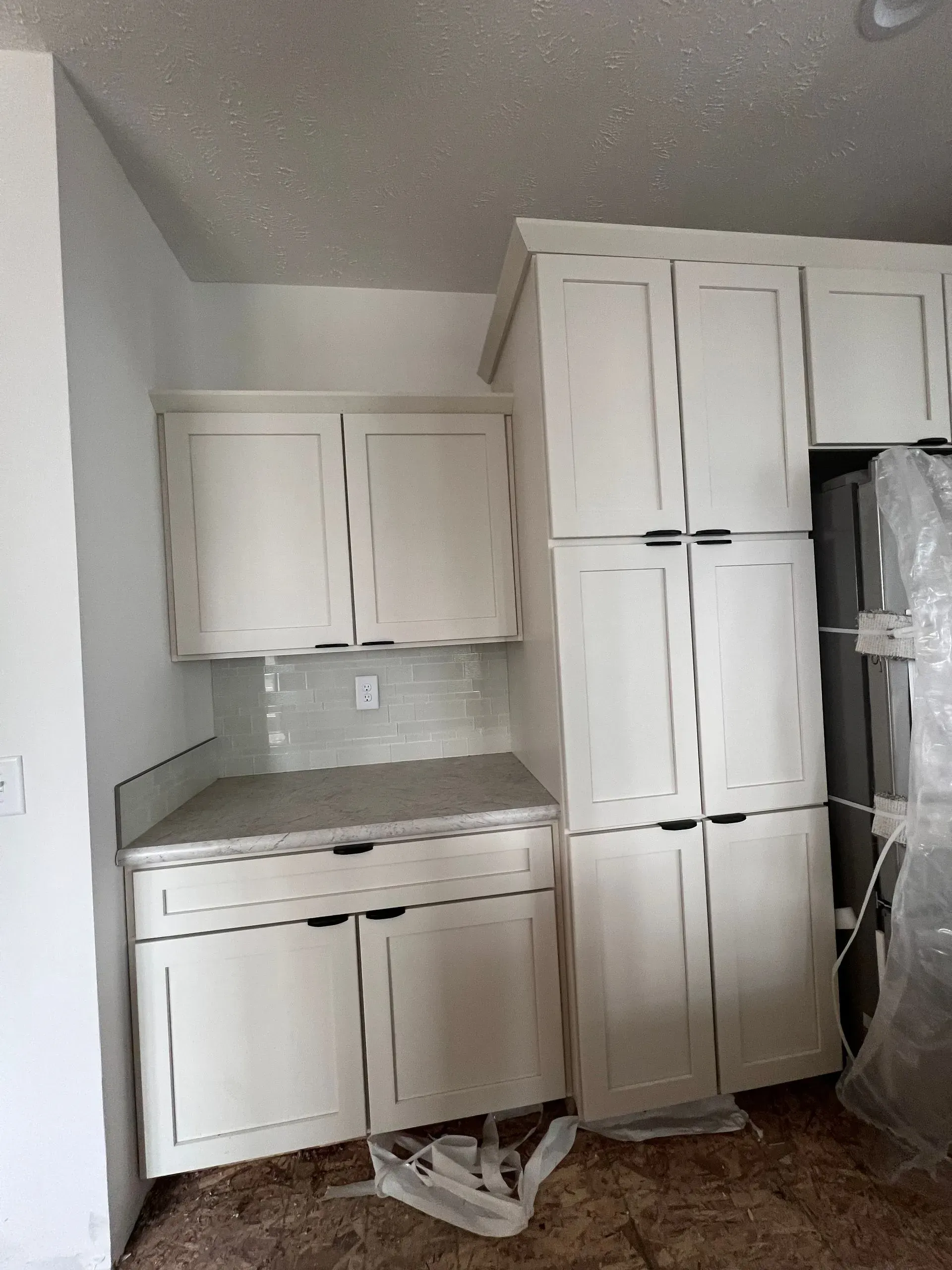 White kitchen cabinets with gray countertops and backsplash; refrigerator partially visible.