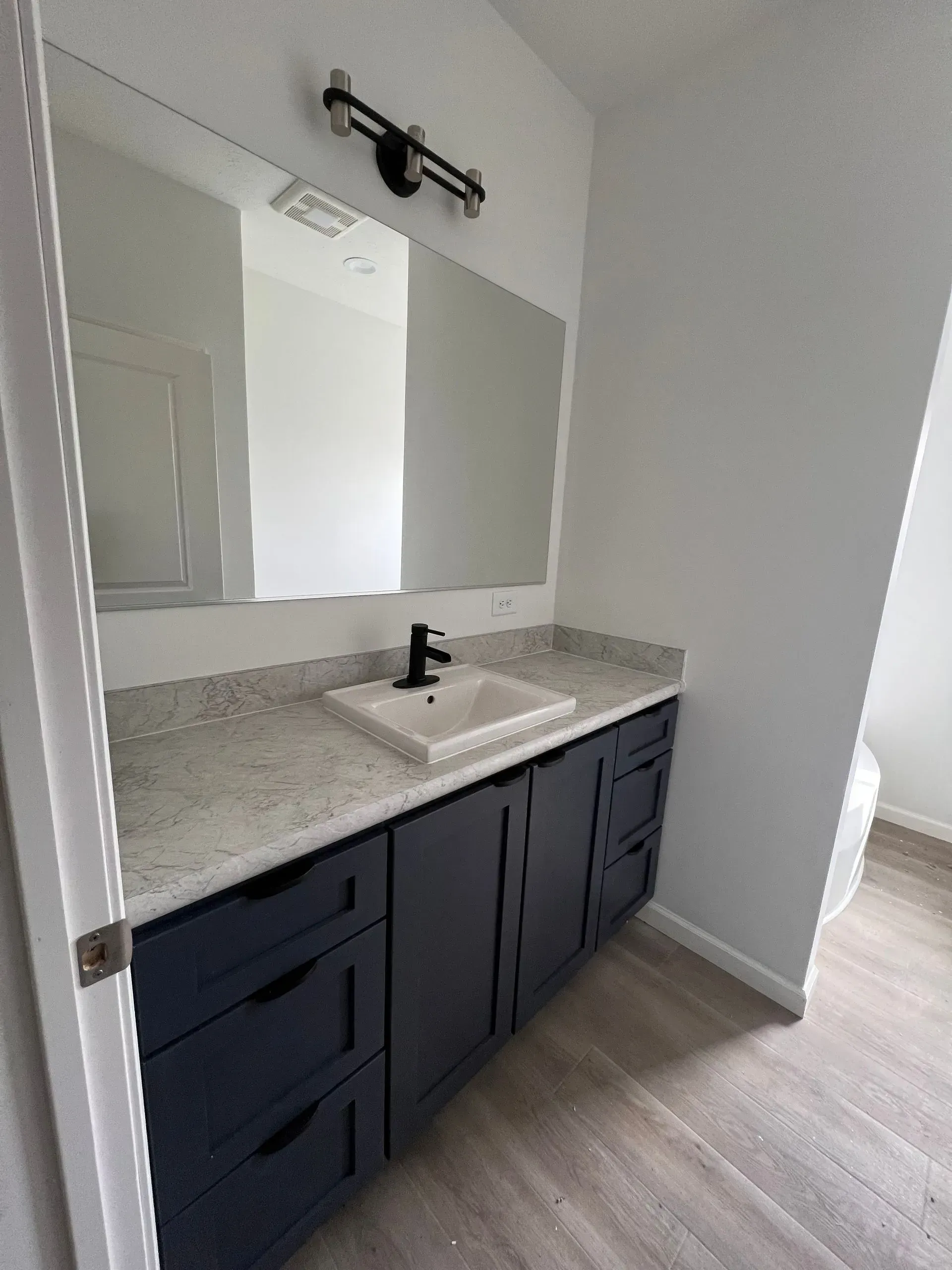 Bathroom with navy blue vanity, white countertop, and large mirror.