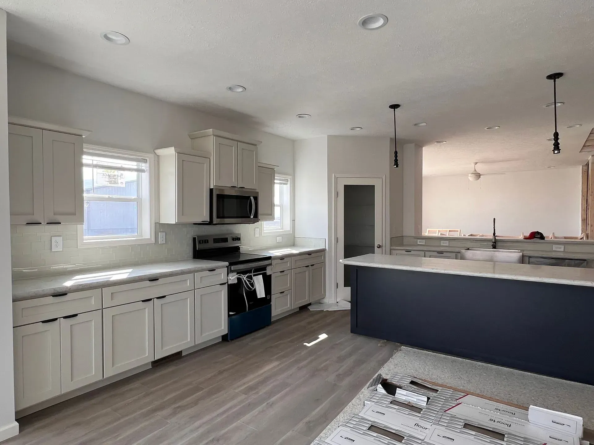 Modern kitchen with gray cabinets, dark blue island, stainless steel appliances, and light wood floors.