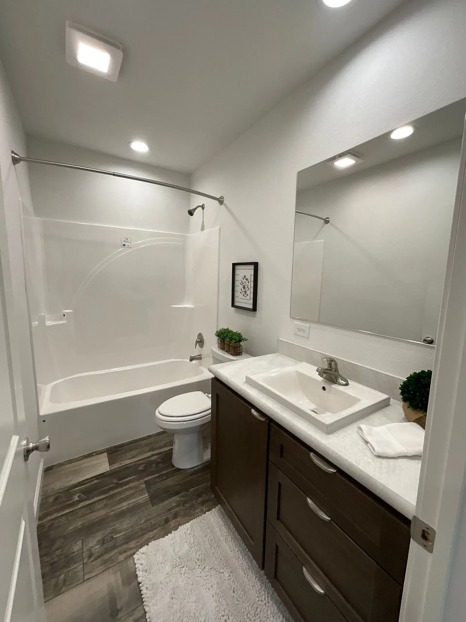 Bathroom with white tub, toilet, and vanity with dark wood cabinets and a grey and white rug.