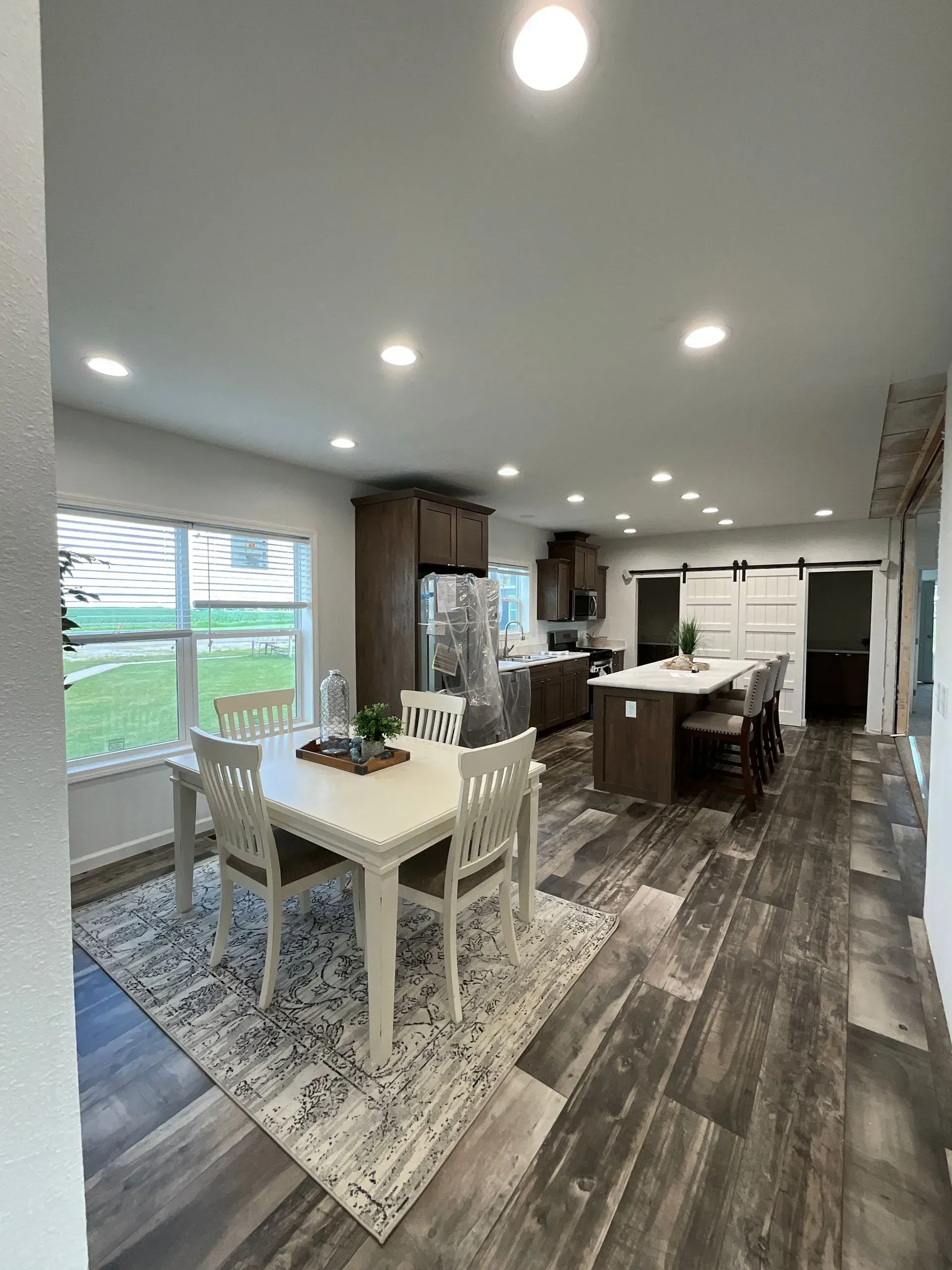 Interior view of a kitchen and dining area with wood-look flooring, a white table, and a kitchen island.