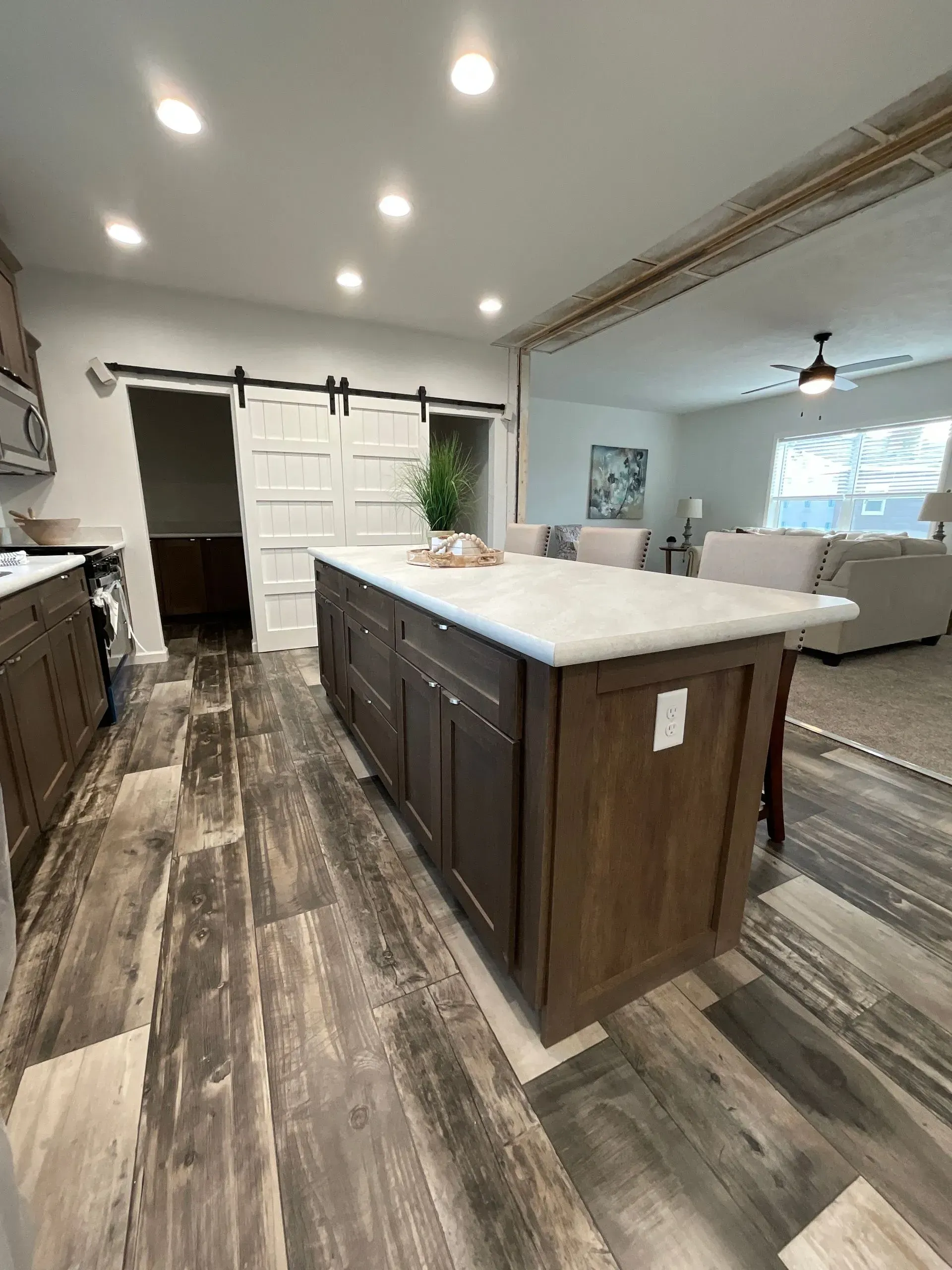 Kitchen with wooden floor, island, and cabinets. Sliding barn door to the left, and open view to the living area.