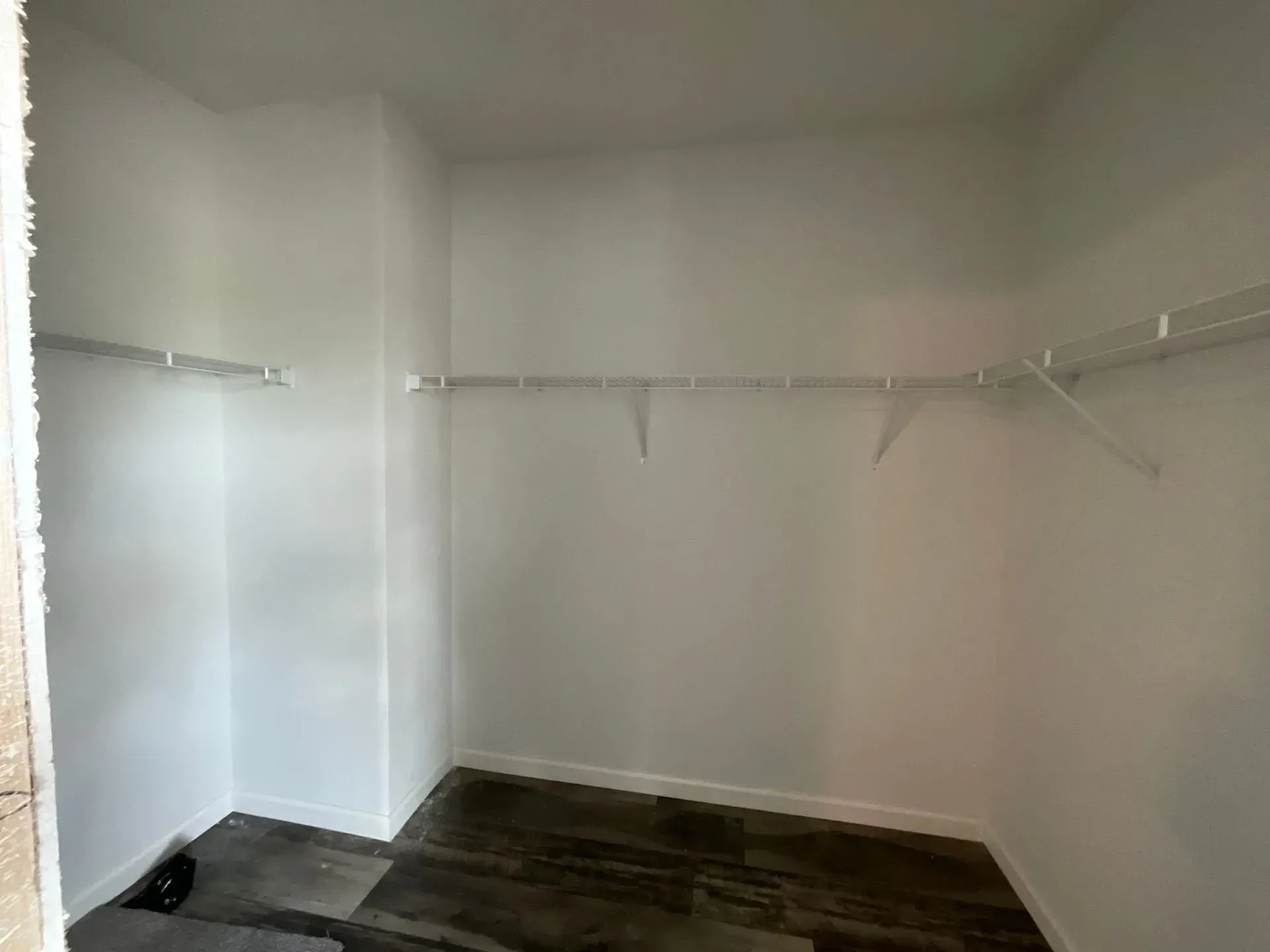 Empty, white-walled closet with wire shelving and dark wood-look flooring.
