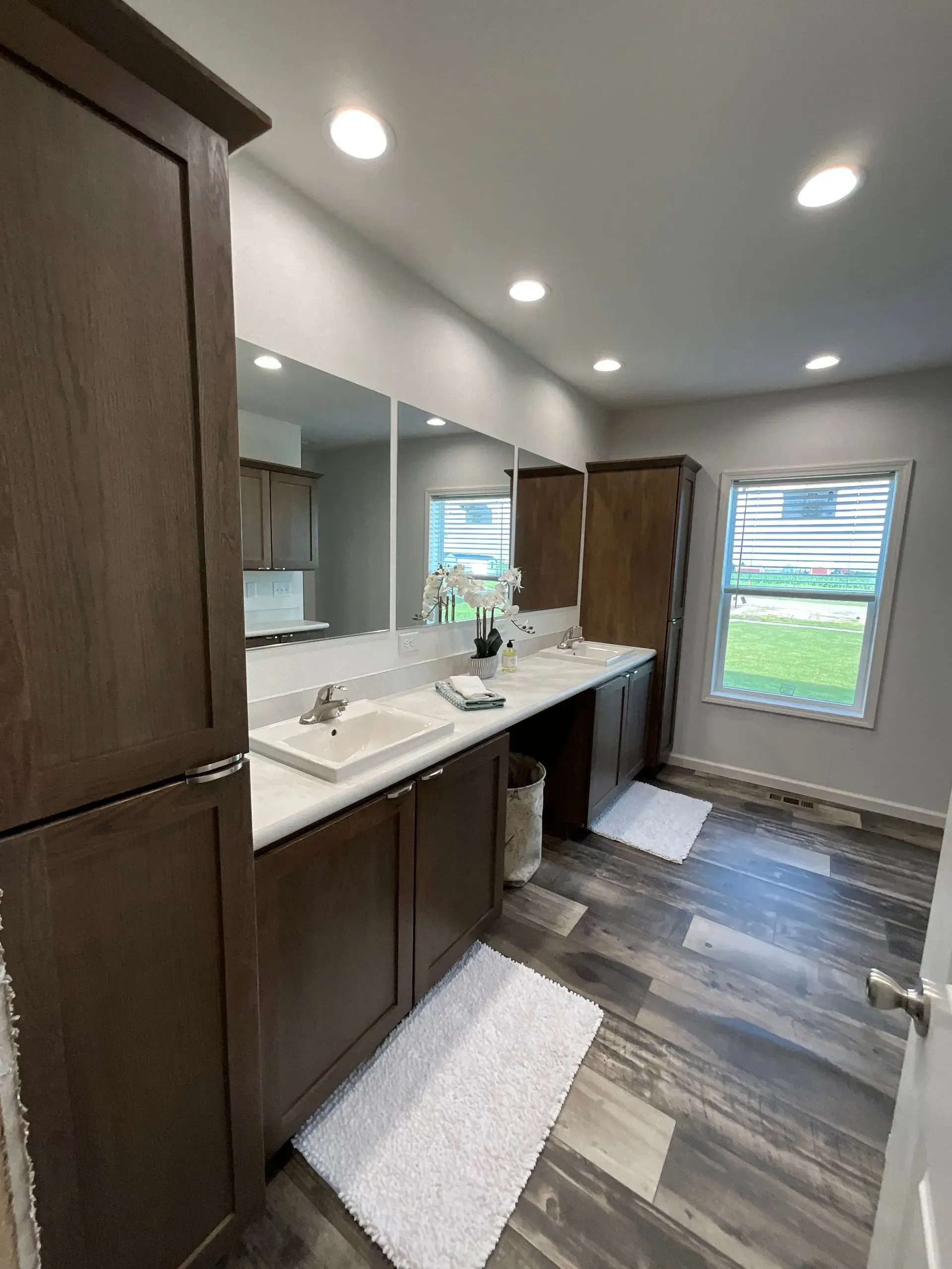 Bathroom with dark brown cabinets, dual sinks, large mirror, and gray flooring.