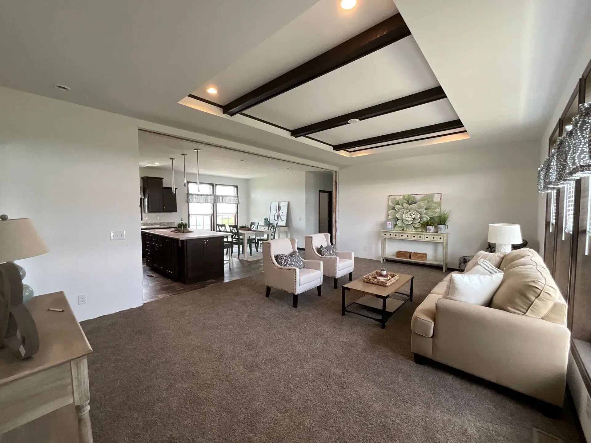 Spacious living room with brown carpet, light-colored sofa, and a view into the kitchen.
