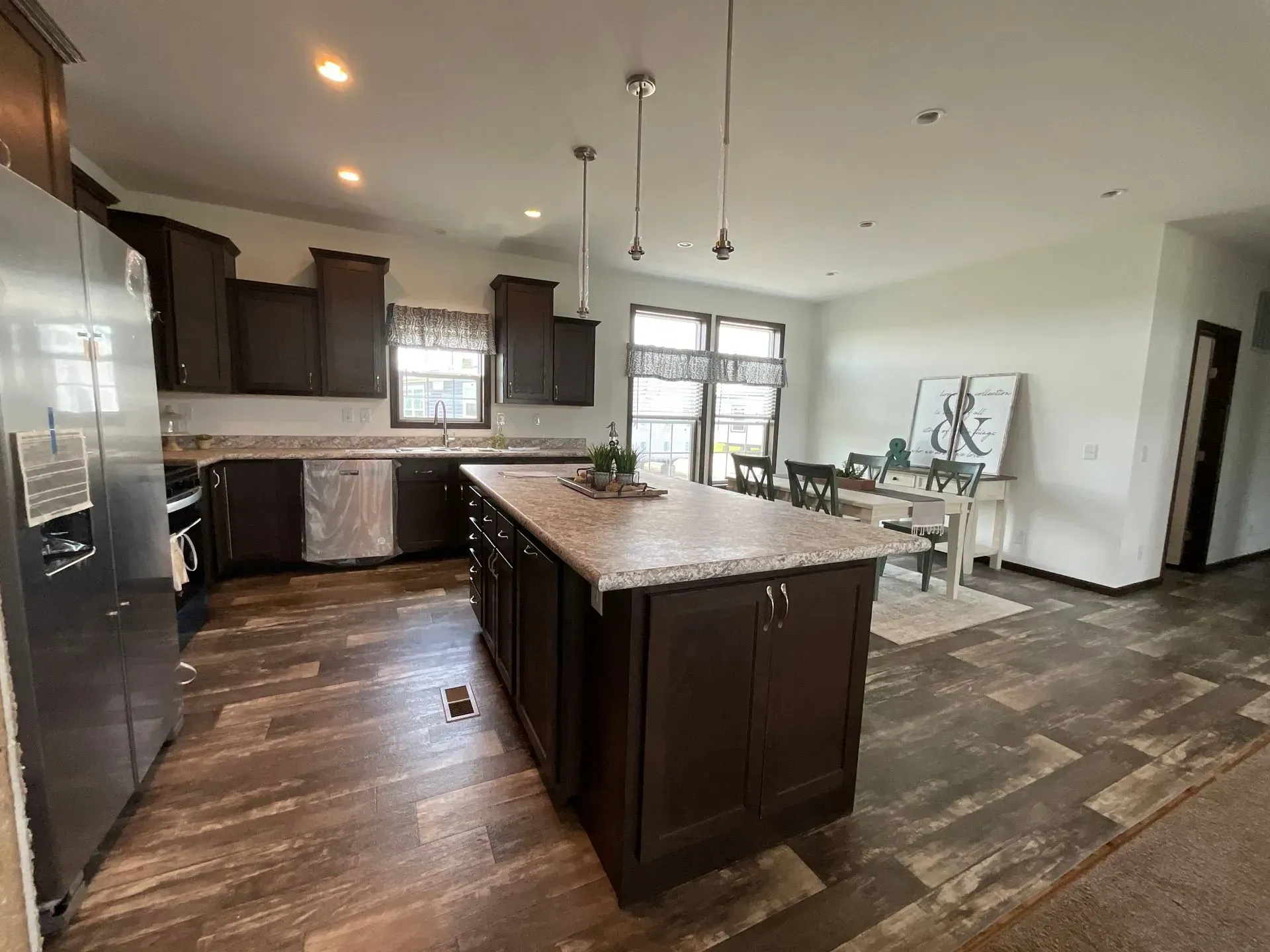 Modern kitchen with dark cabinetry, large island, and dining area with hardwood floors.