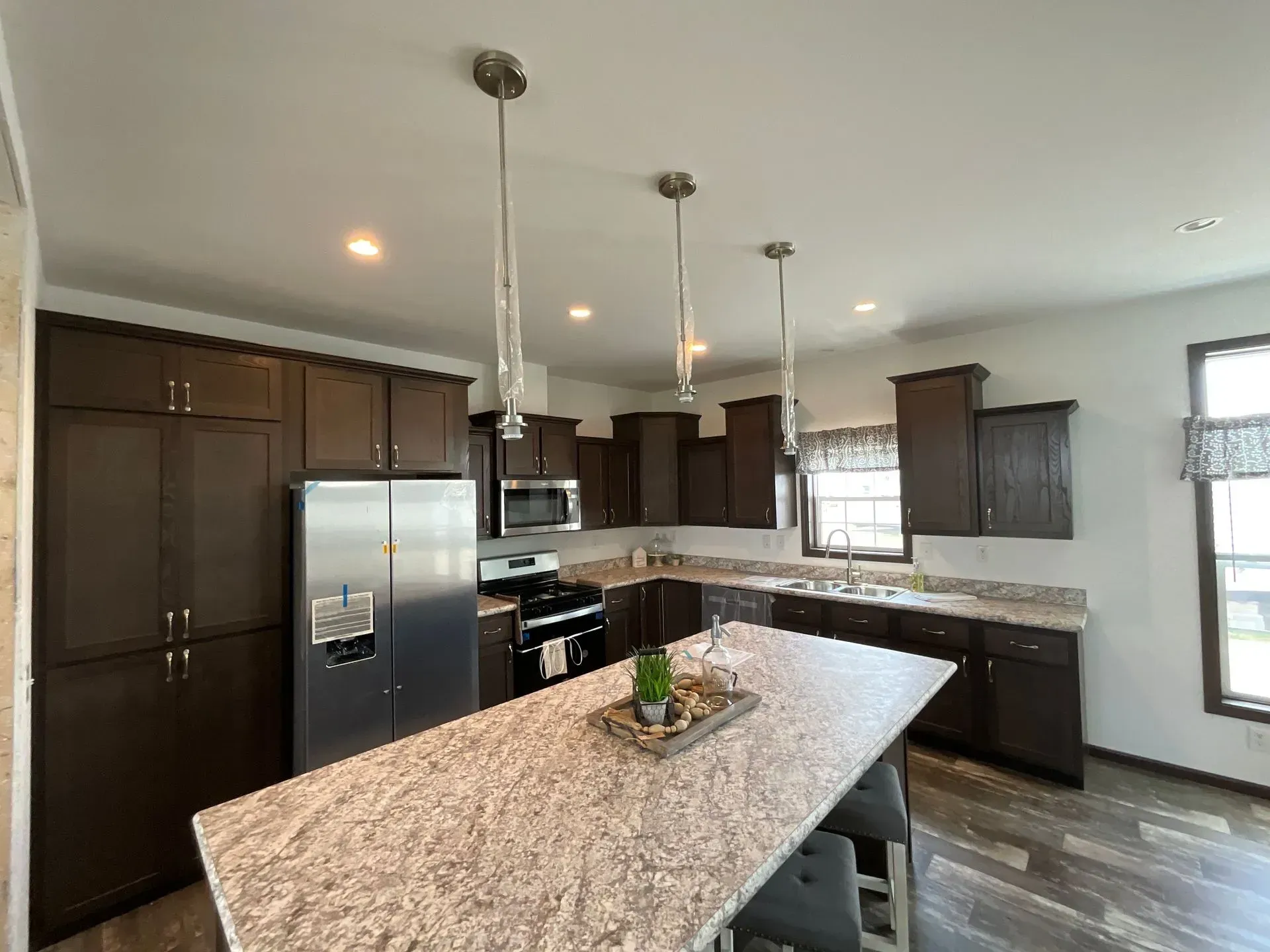 Modern kitchen with dark brown cabinets, stainless steel appliances, and large island with pendant lights.