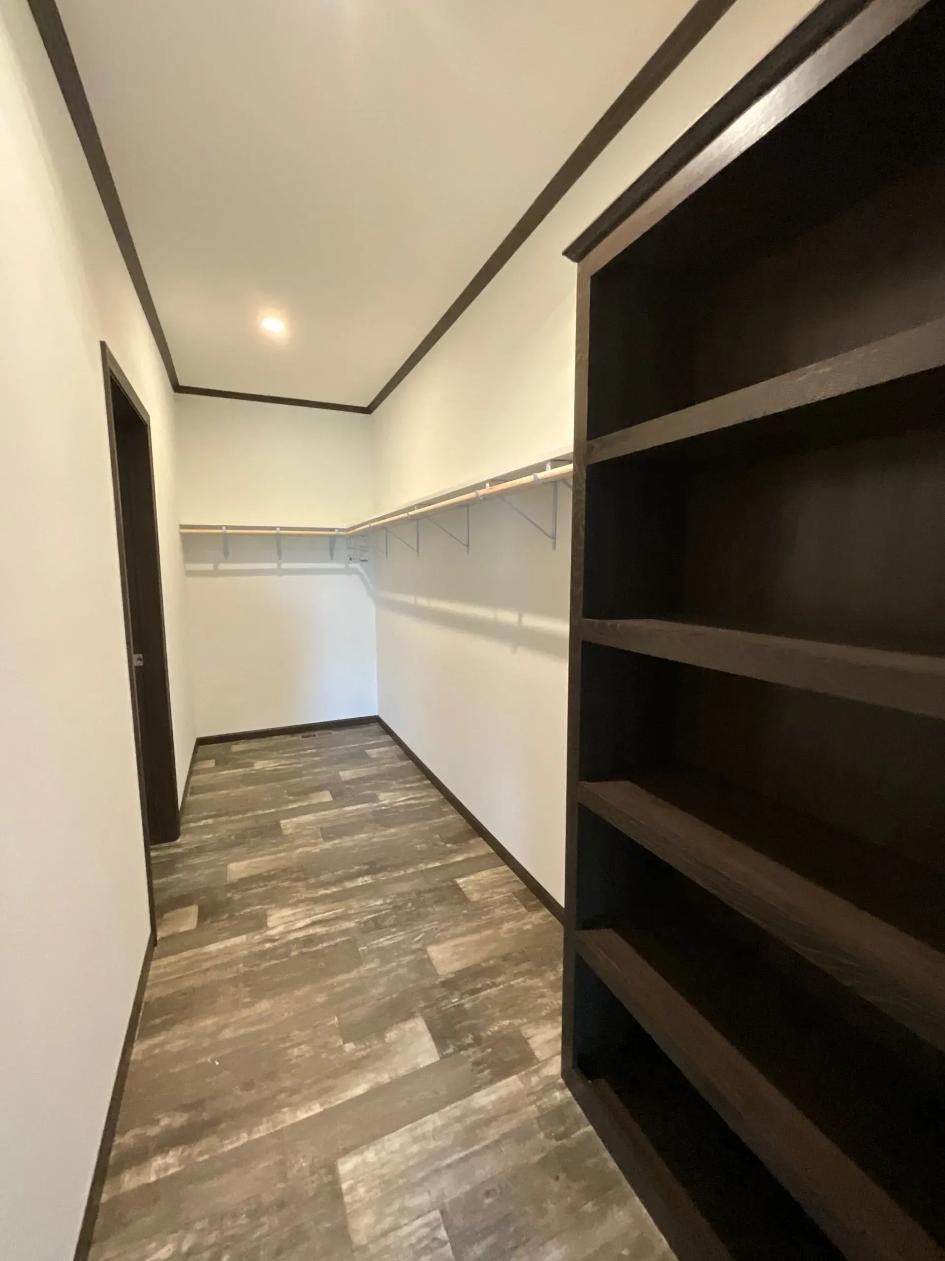 Walk-in closet with dark brown shelving, white walls, and wood-look flooring.