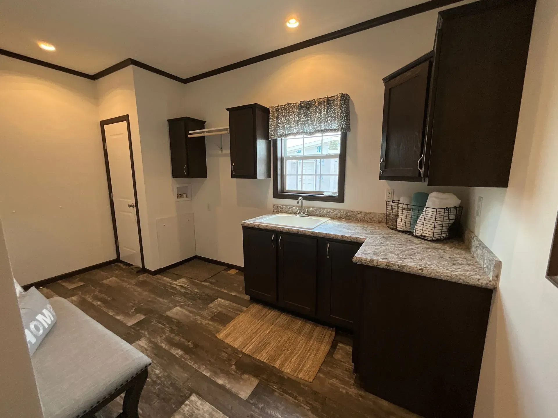 A laundry room with dark cabinets, a sink, a window, and wood-look flooring.
