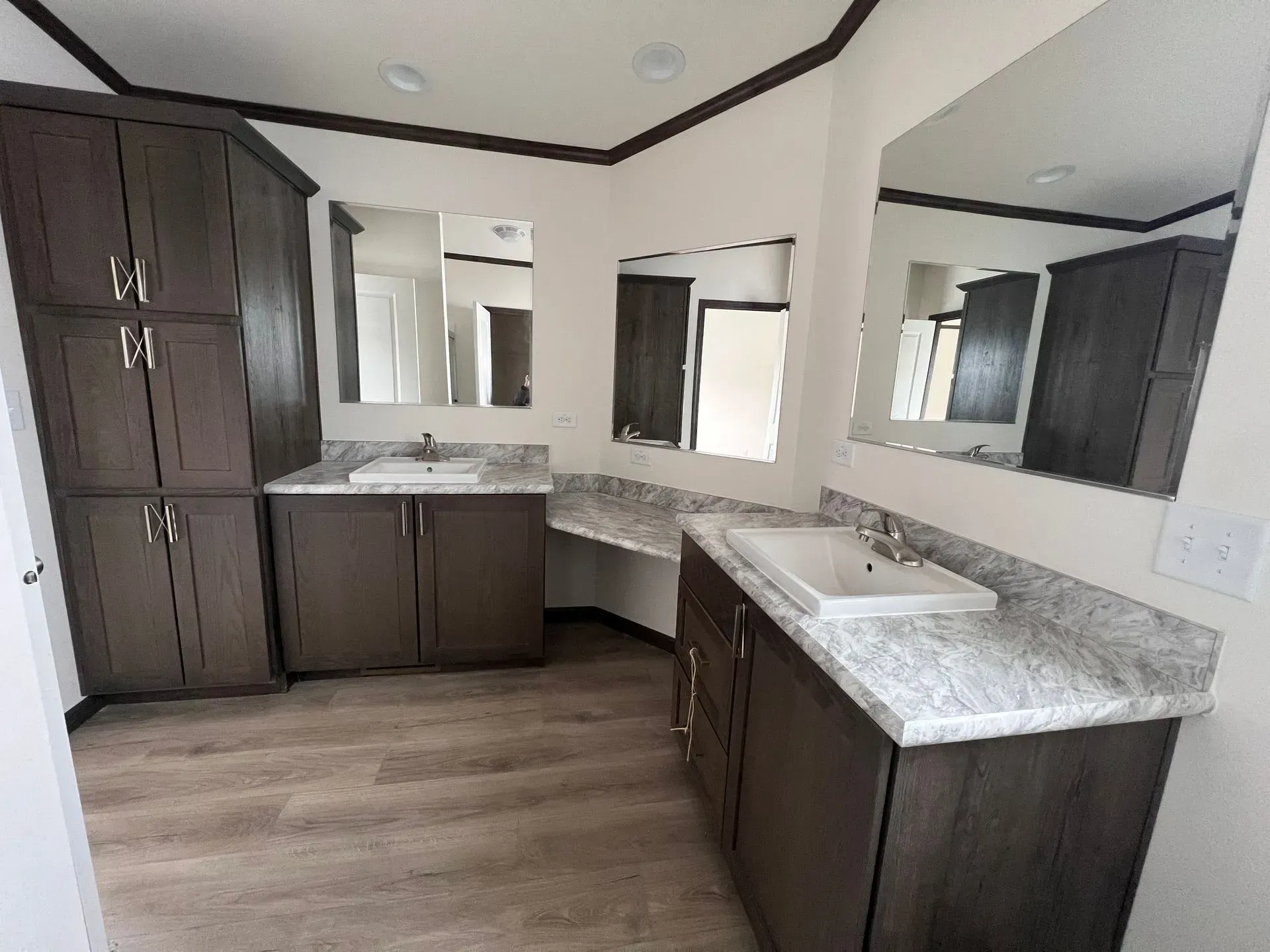 Bathroom with dark brown cabinetry, light countertops, and large mirrors.