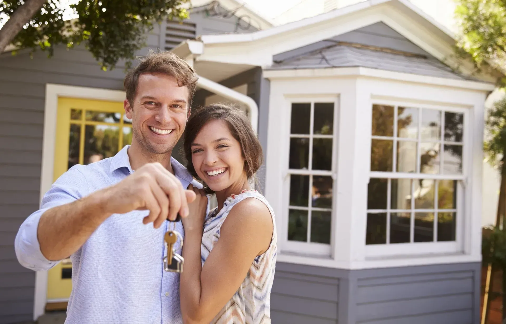 Couple holding keys in front of their new house; smiling.