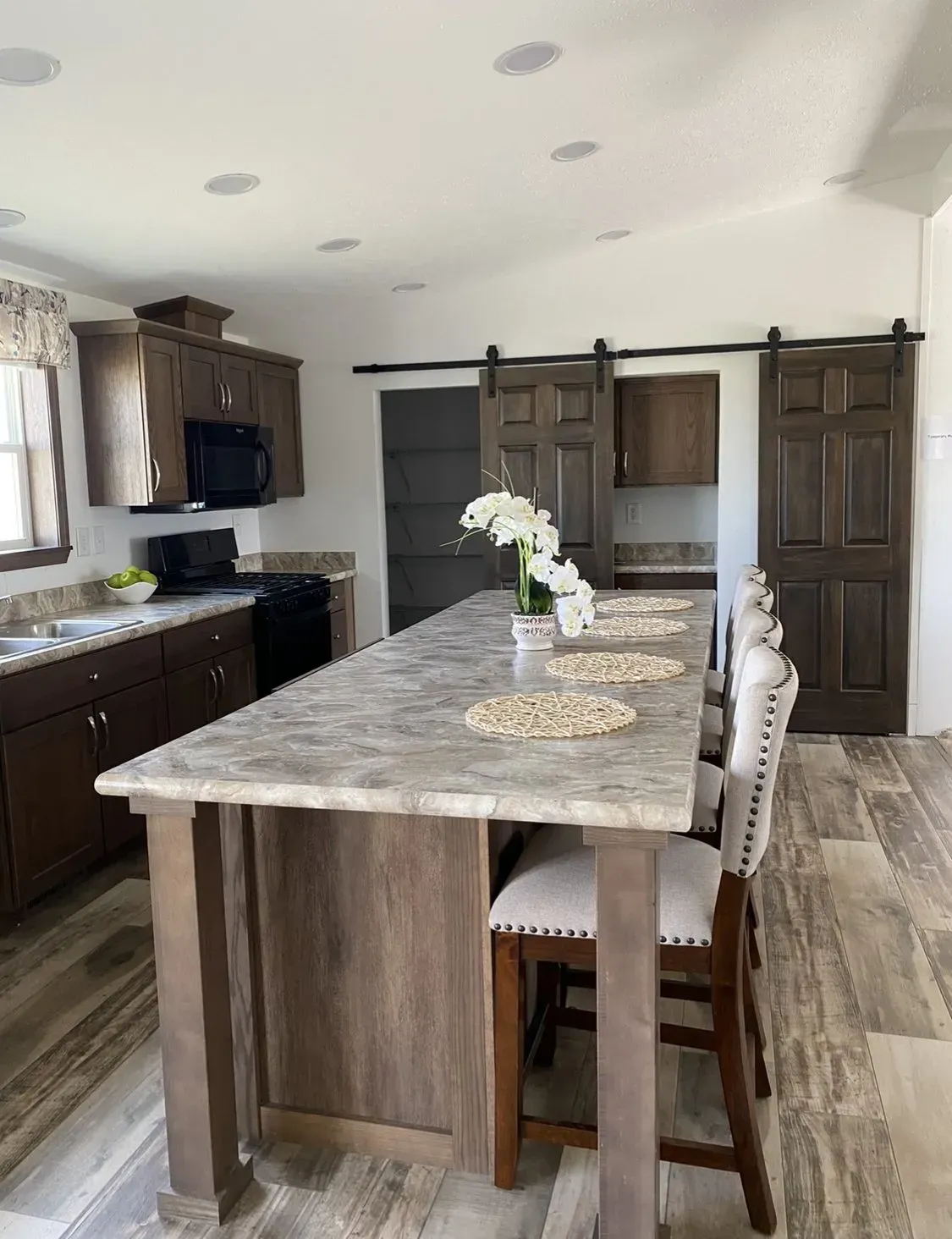 Kitchen with dark brown cabinets, large island with bar seating, and sliding barn doors.