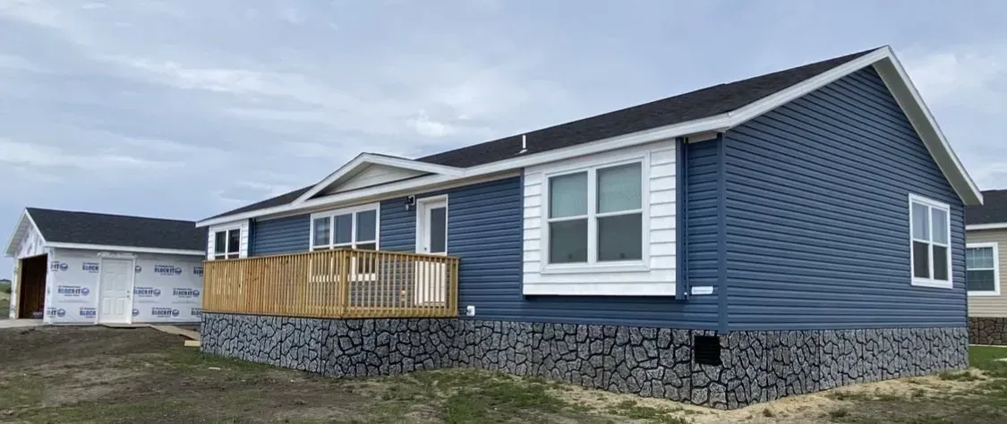 Blue house with stone skirting and wooden deck. A garage is in the background. Overcast sky.