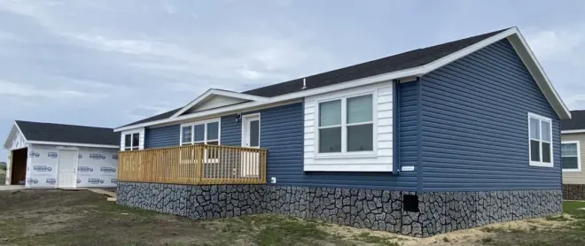 Blue-sided house with a wooden deck and stone foundation under a cloudy sky.