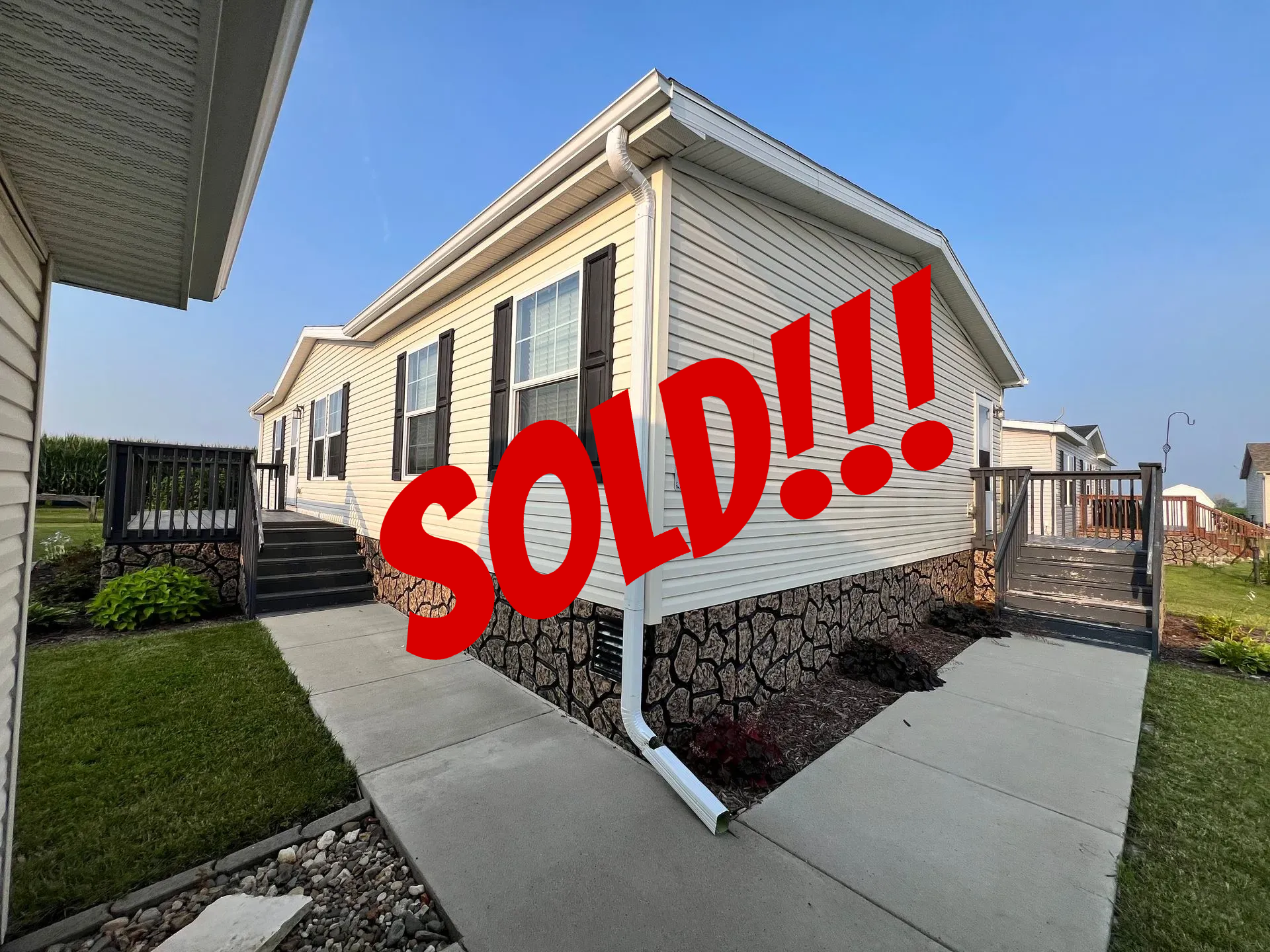 Beige and brown house with black shutters, walkway, and a dark brown fence.