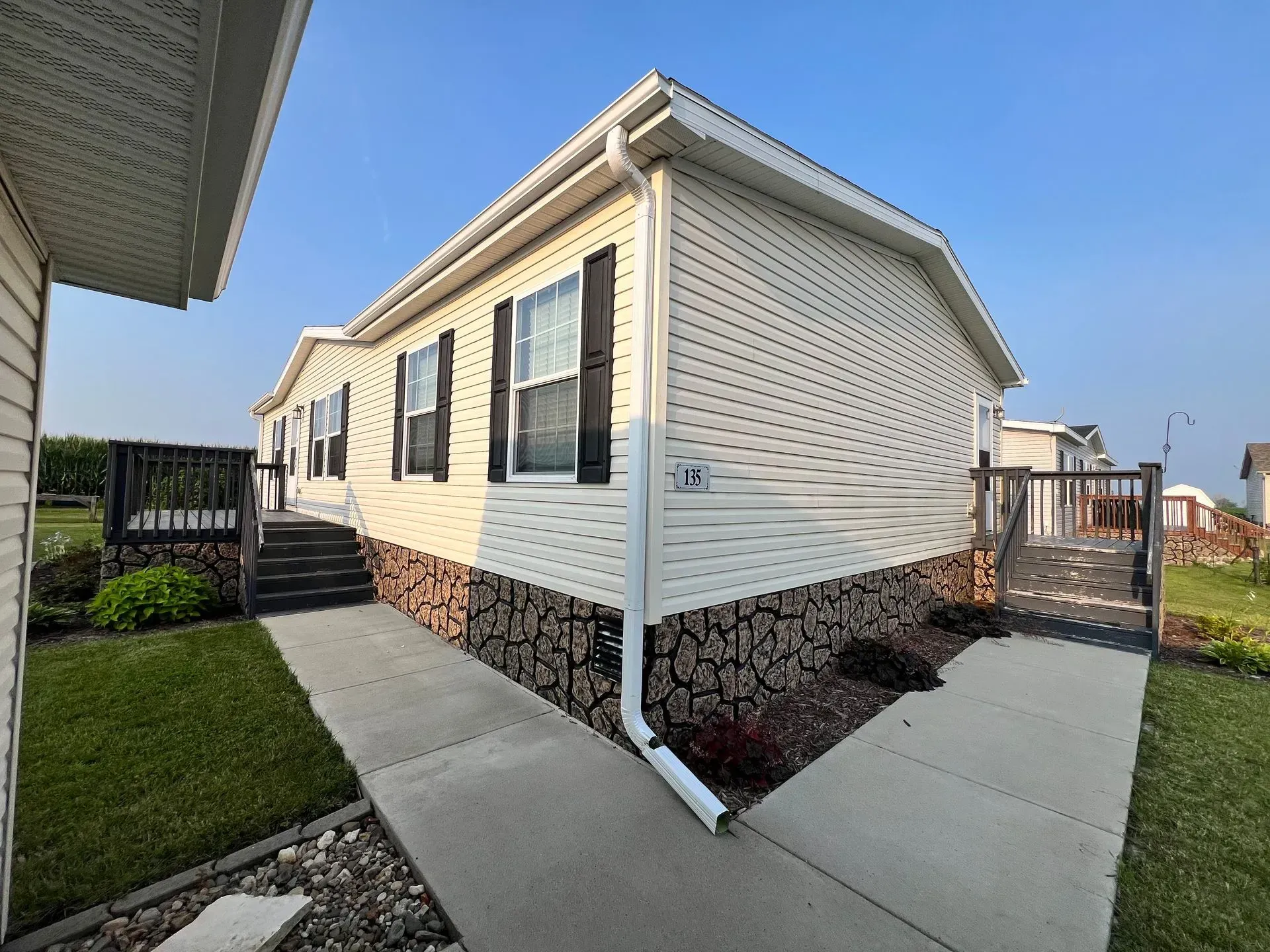 Beige and brown house with black shutters, walkway, and a dark brown fence.