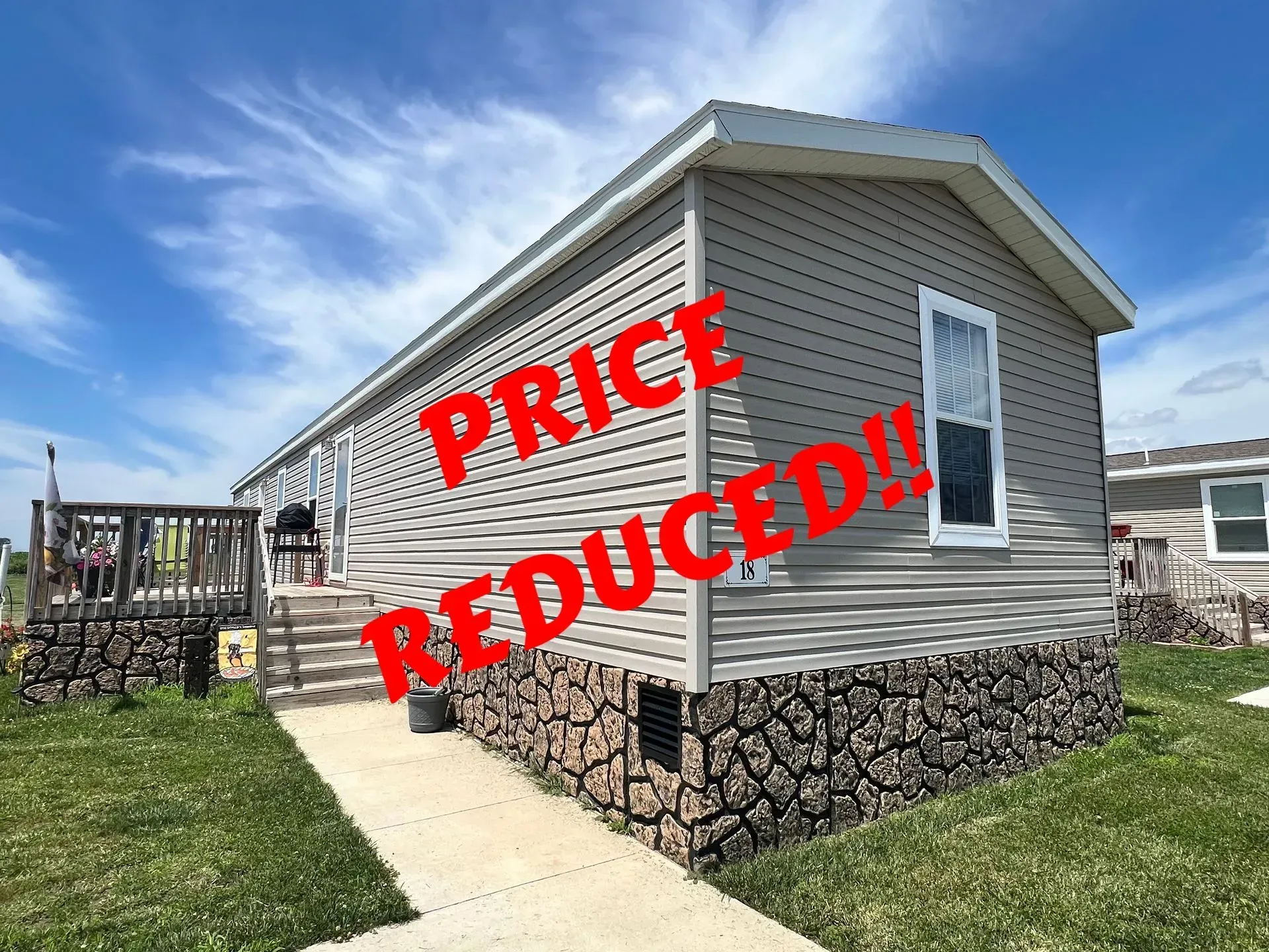 Price reduced! Gray manufactured home with stone base. Sunny outdoor setting.