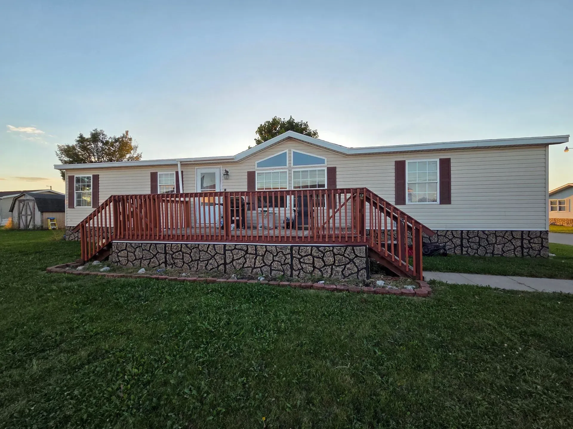Mobile home with a wooden deck and brown shutters; green lawn in front.