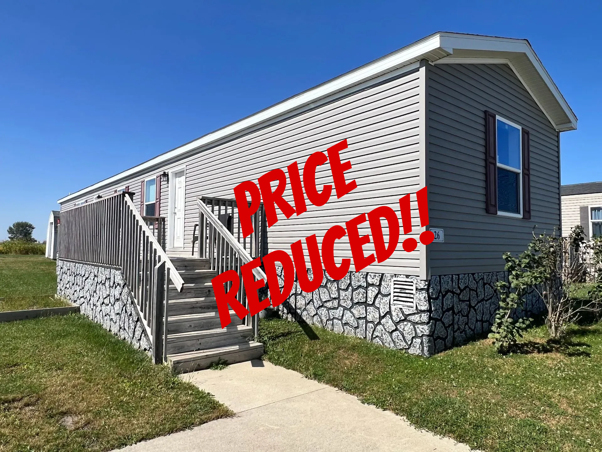 Gray and white mobile home with steps and stone accents, blue sky background.