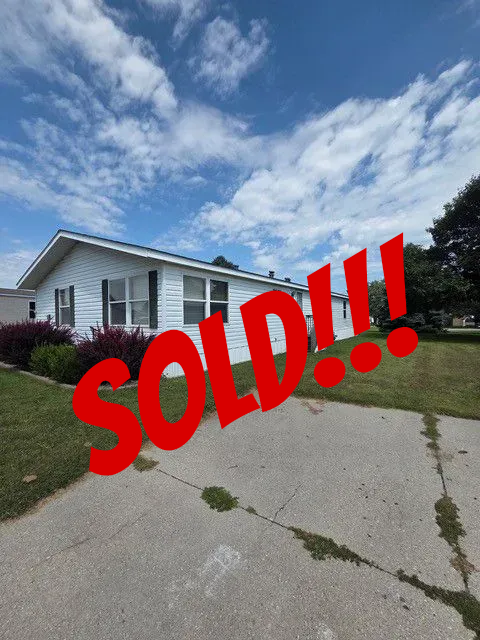 White house with light blue sky, dark pink bushes, and a concrete driveway.